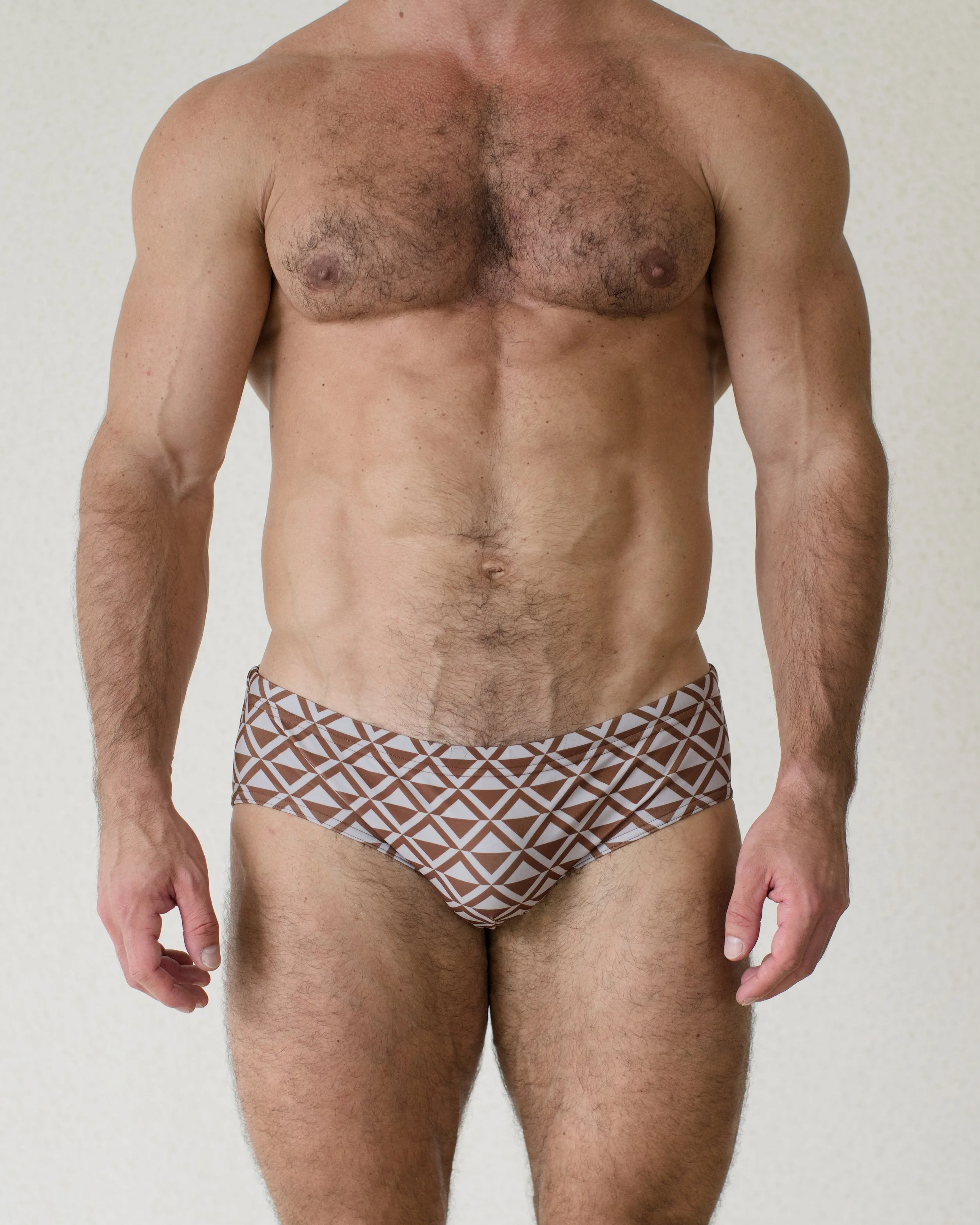 Man is seen from front wearing brown geometric patterned Latte Paradigm Swim Brief from Aronik Swim Paradigm Collection