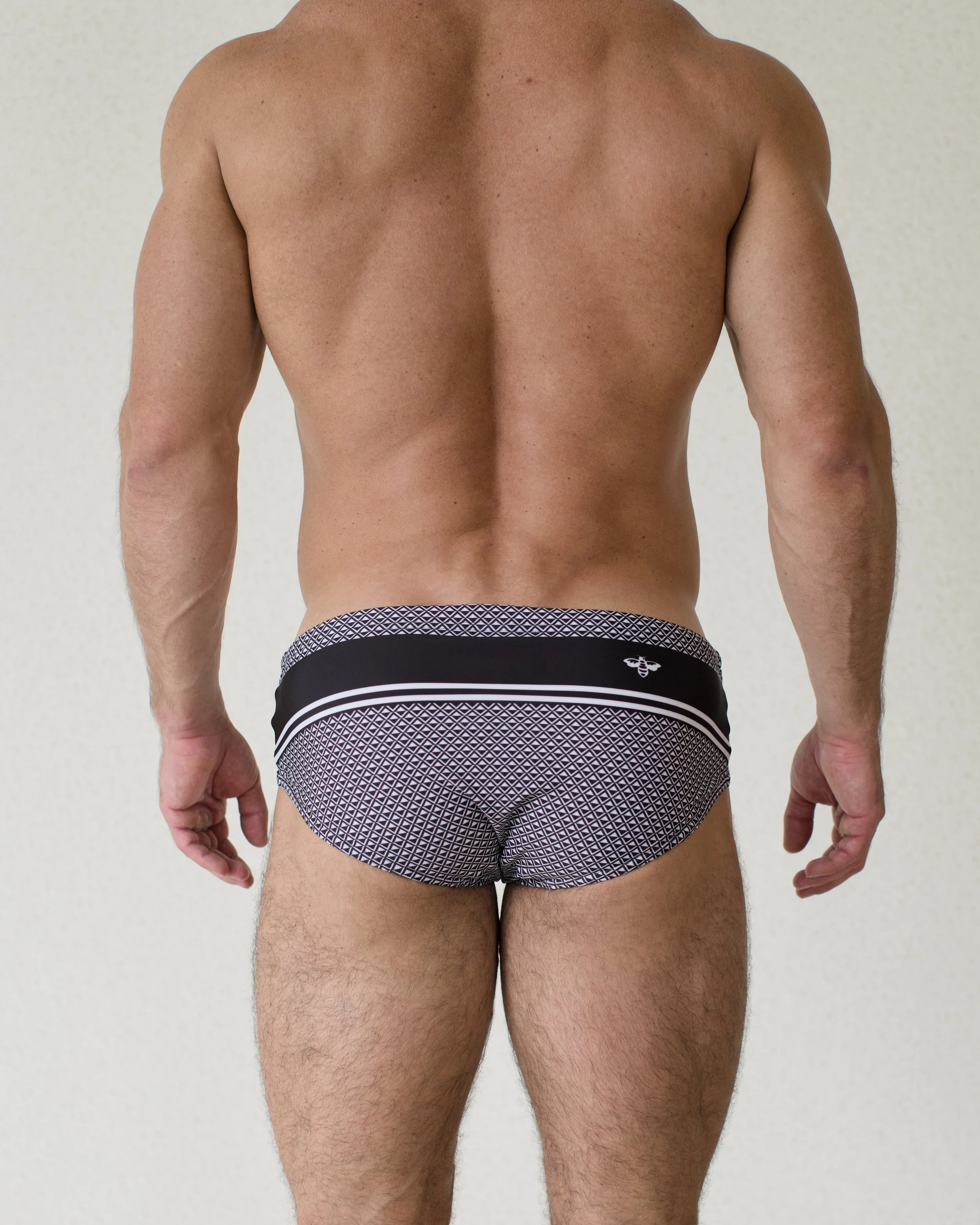 Man seen from back wearing Bastion swim brief featuring bold black geometric print from Aronik Swim Paradigm Collection