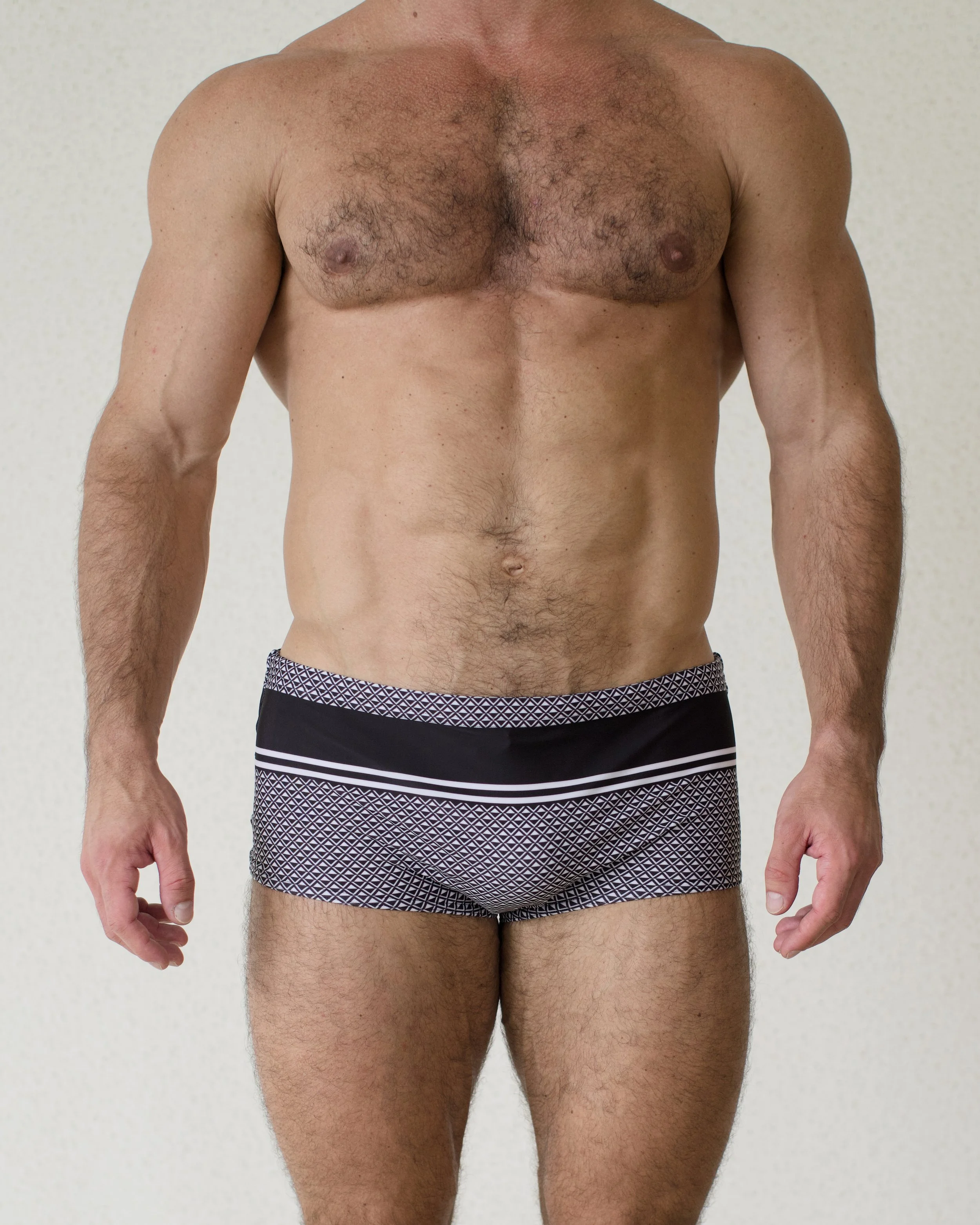 Man seen from front wearing Bastion swim sunga featuring bold black geometric print from Aronik Swim Paradigm Collection