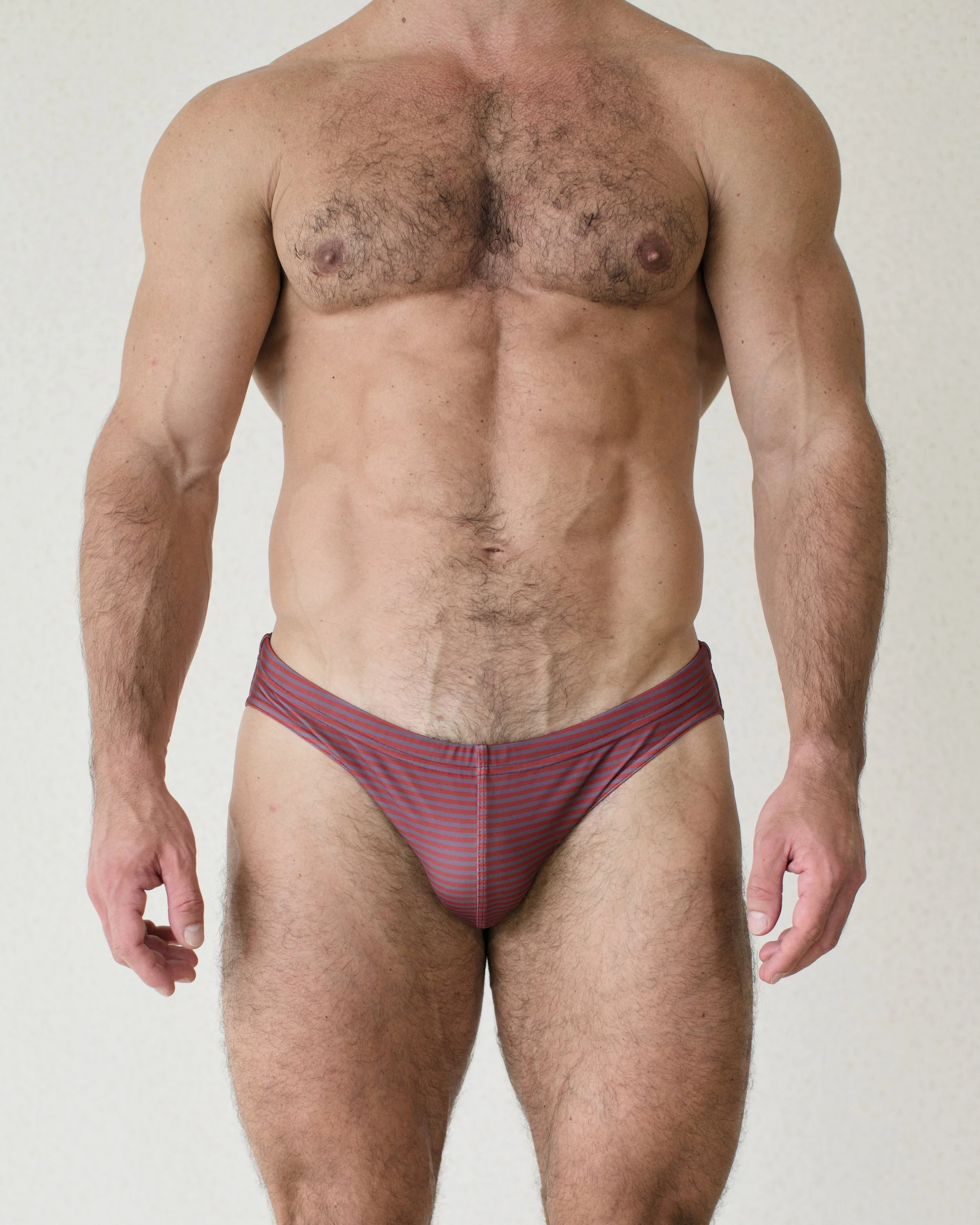 Man seen from the front wearing red and brown striped Out of Office City swim brief from Aronik Swim Paradigm collection