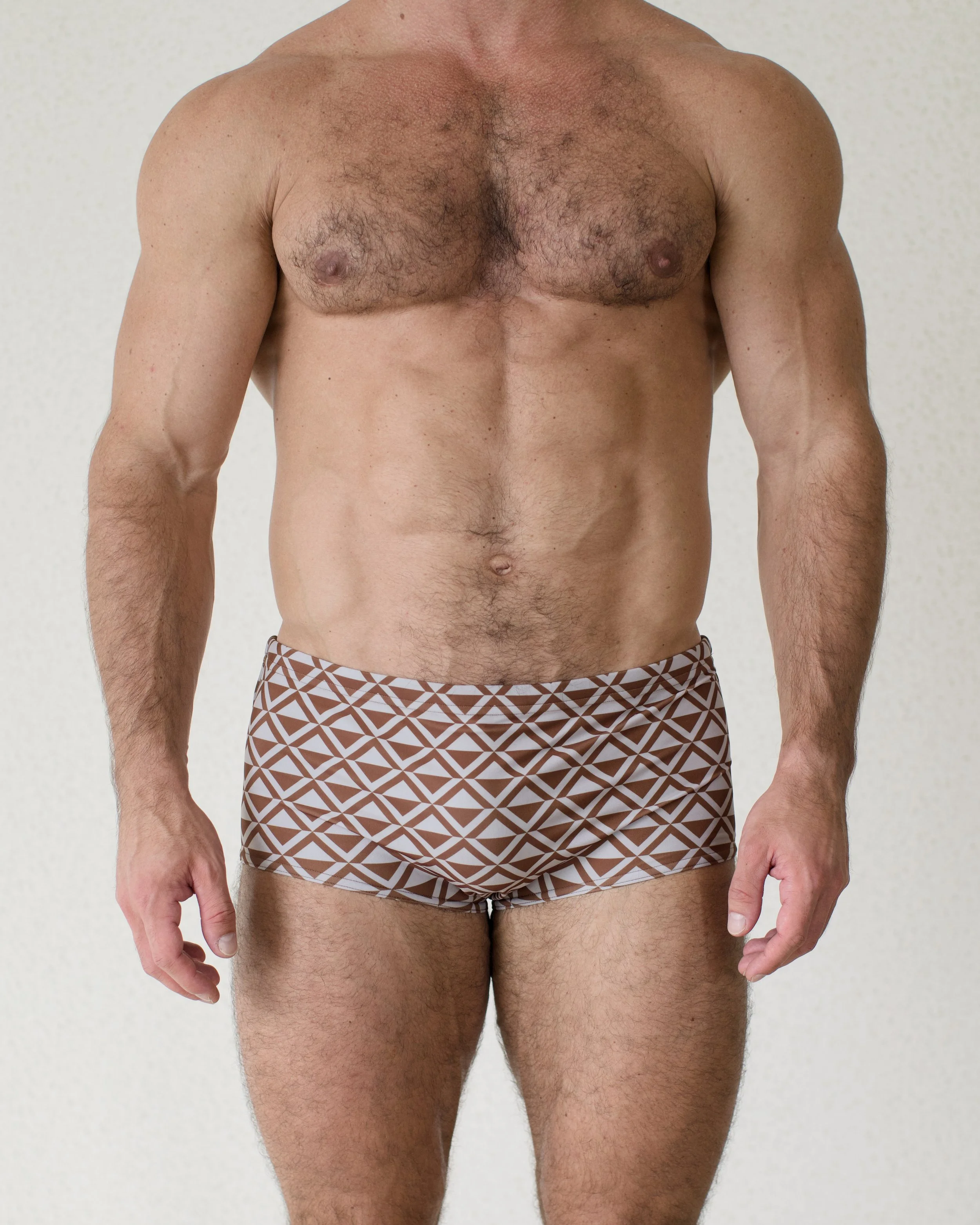 Man seen from front wearing Latte Paradigm swim sunga featuring brown geometric print from Aronik Swim Paradigm Collection
