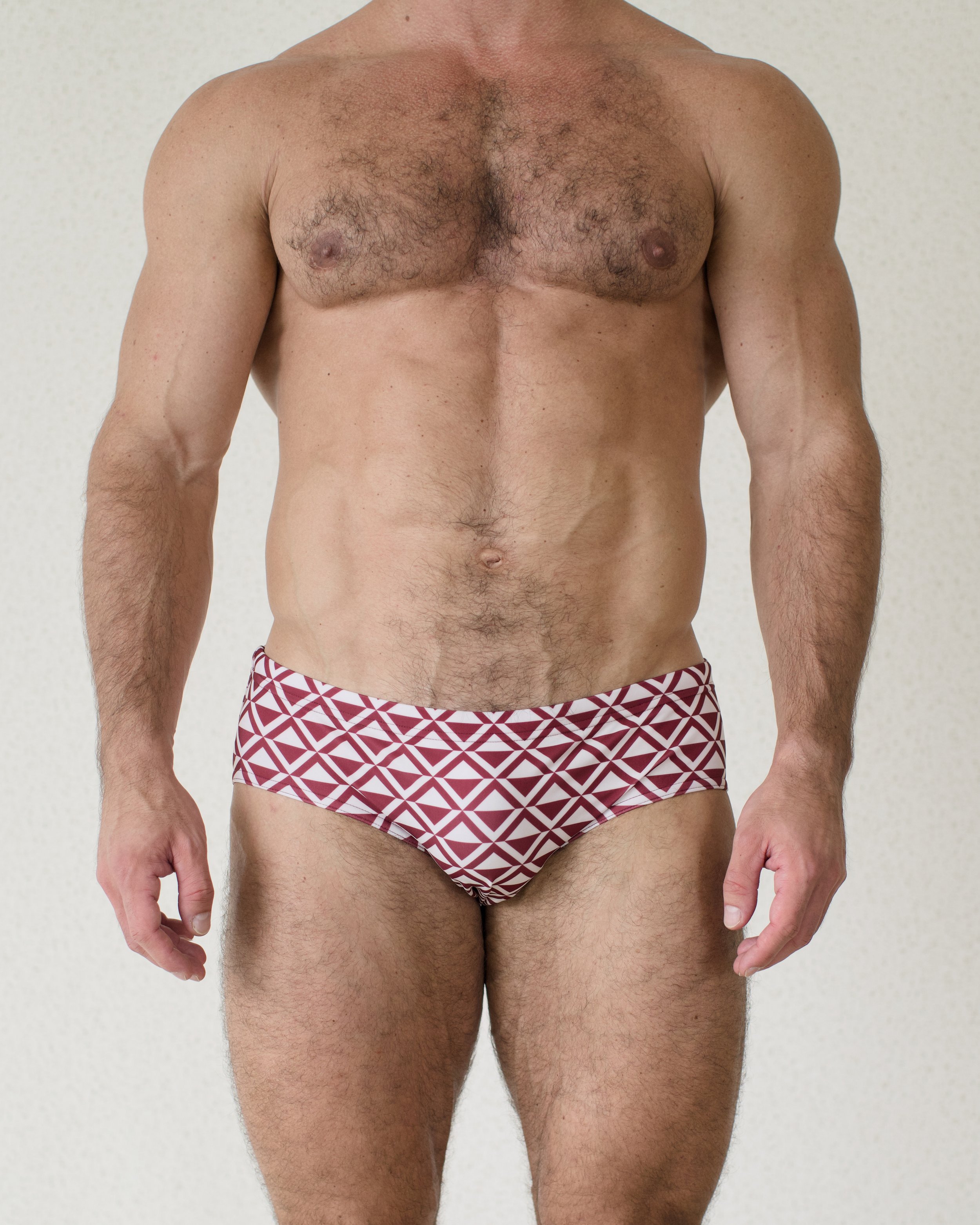 Man is seen from front wearing red geometric patterned Cherry Paradigm Swim Brief from Aronik Swim Paradigm Collection