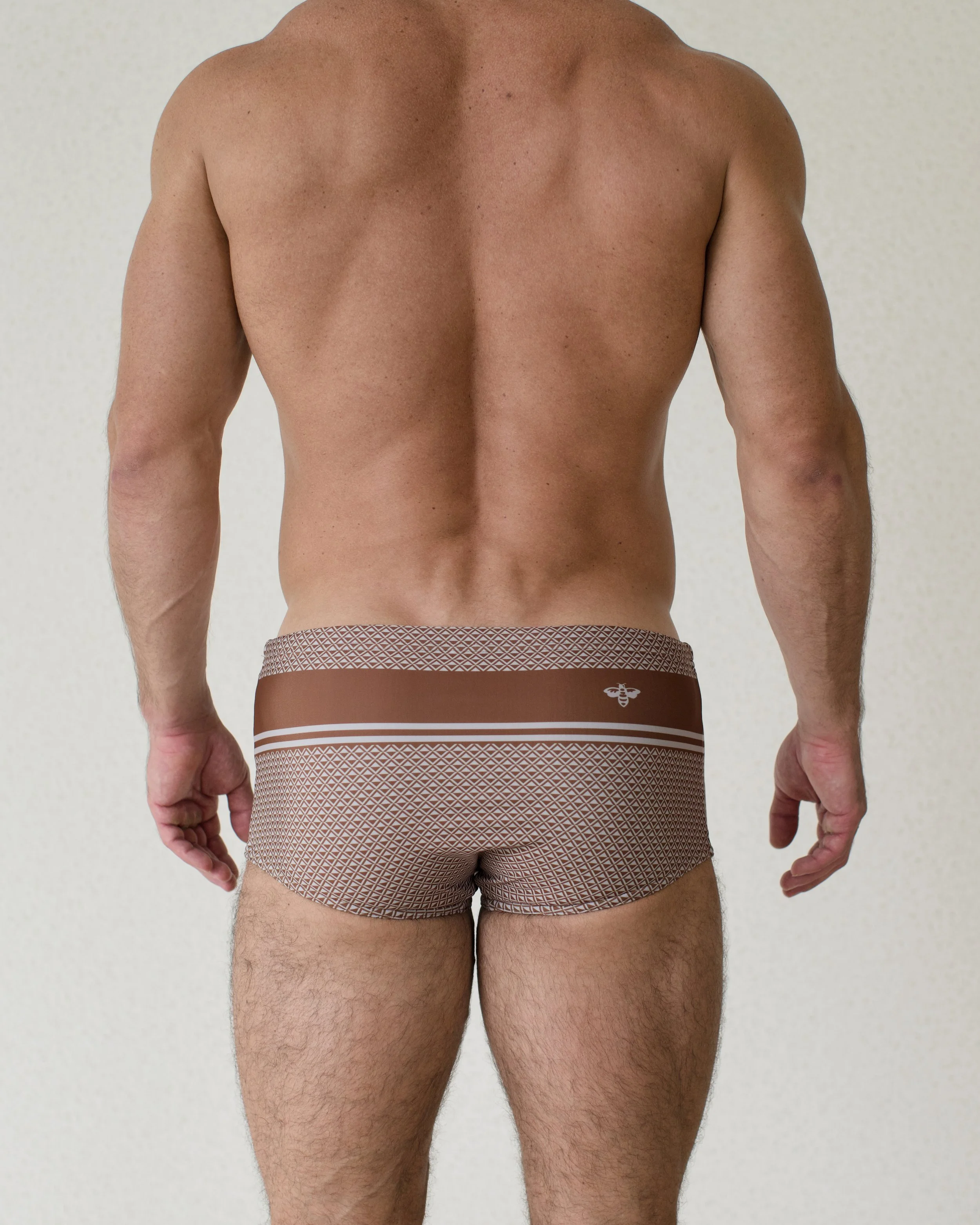 Man seen from back wearing Bastion Cafe swim sunga featuring rich brown geometric print from Aronik Swim Paradigm Collection