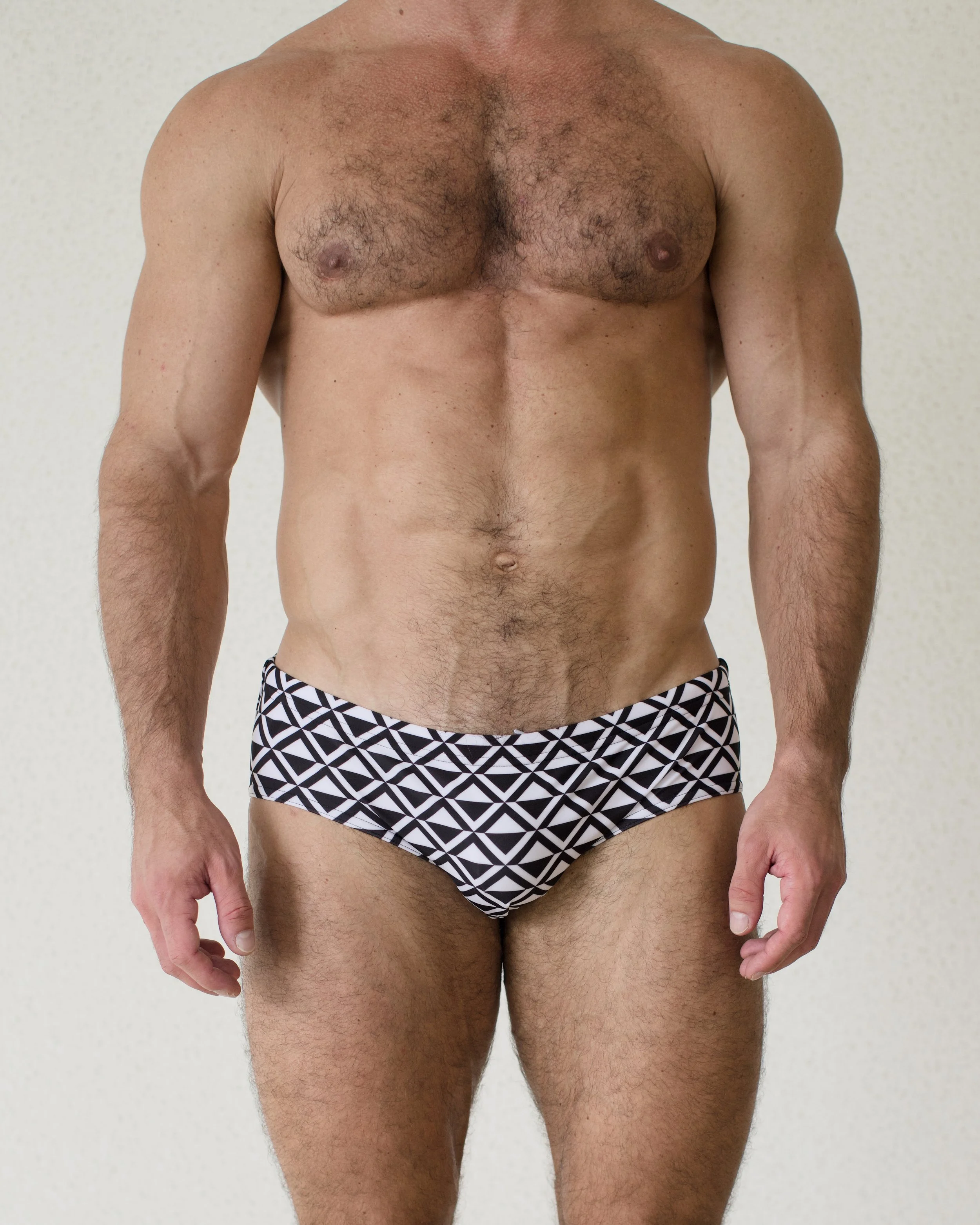 Man is seen from front wearing black geometric patterned Paradigm Swim Brief from Aronik Swim Paradigm Collection