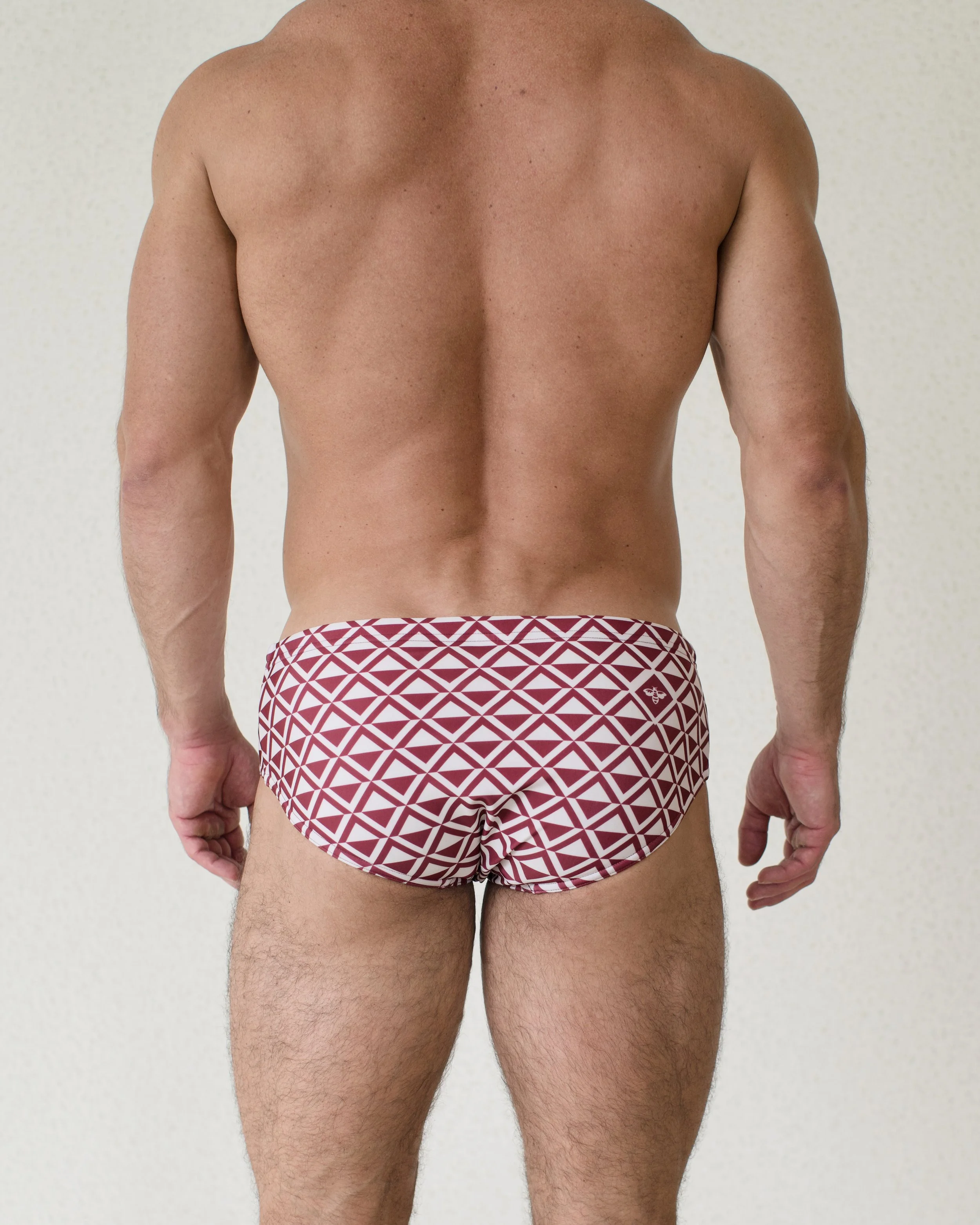 Man is seen from back wearing red geometric patterned Cherry Paradigm Swim Brief from Aronik Swim Paradigm Collection