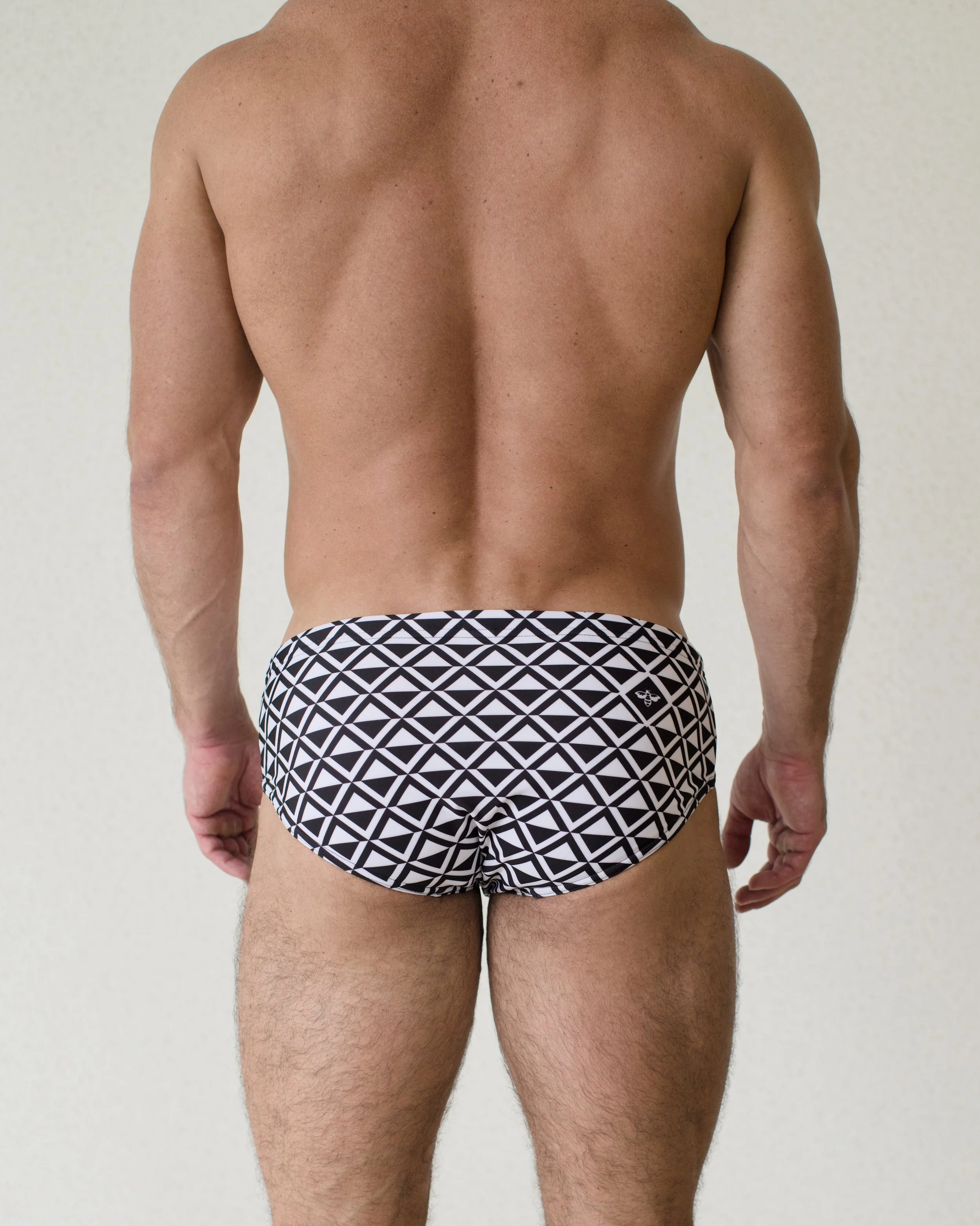 Man is seen from back wearing black geometric patterned Paradigm Swim Brief from Aronik Swim Paradigm Collection