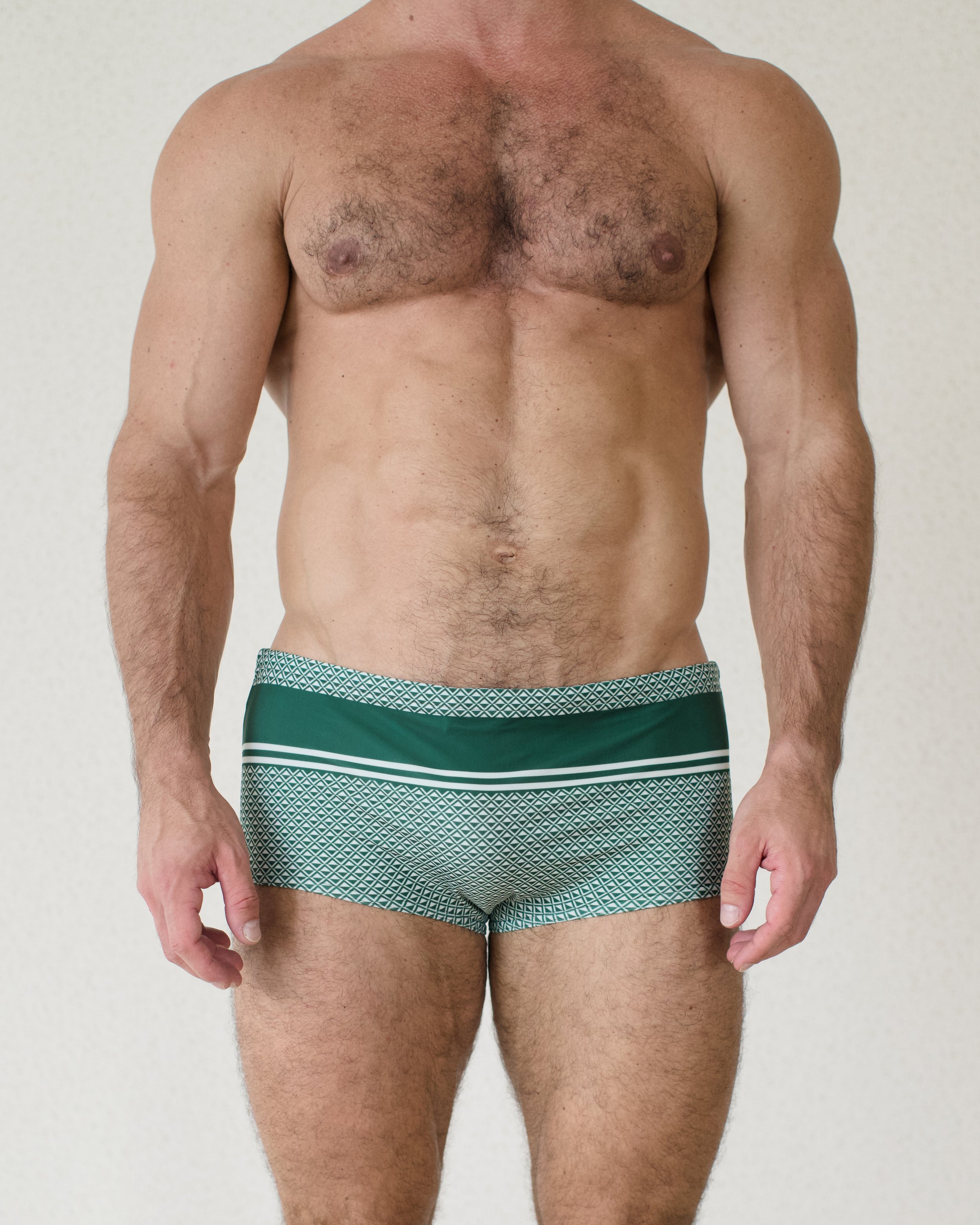 Man seen from front wearing Bastion Prado swim sunga featuring deep green geometric print from Aronik Swim Paradigm Collection