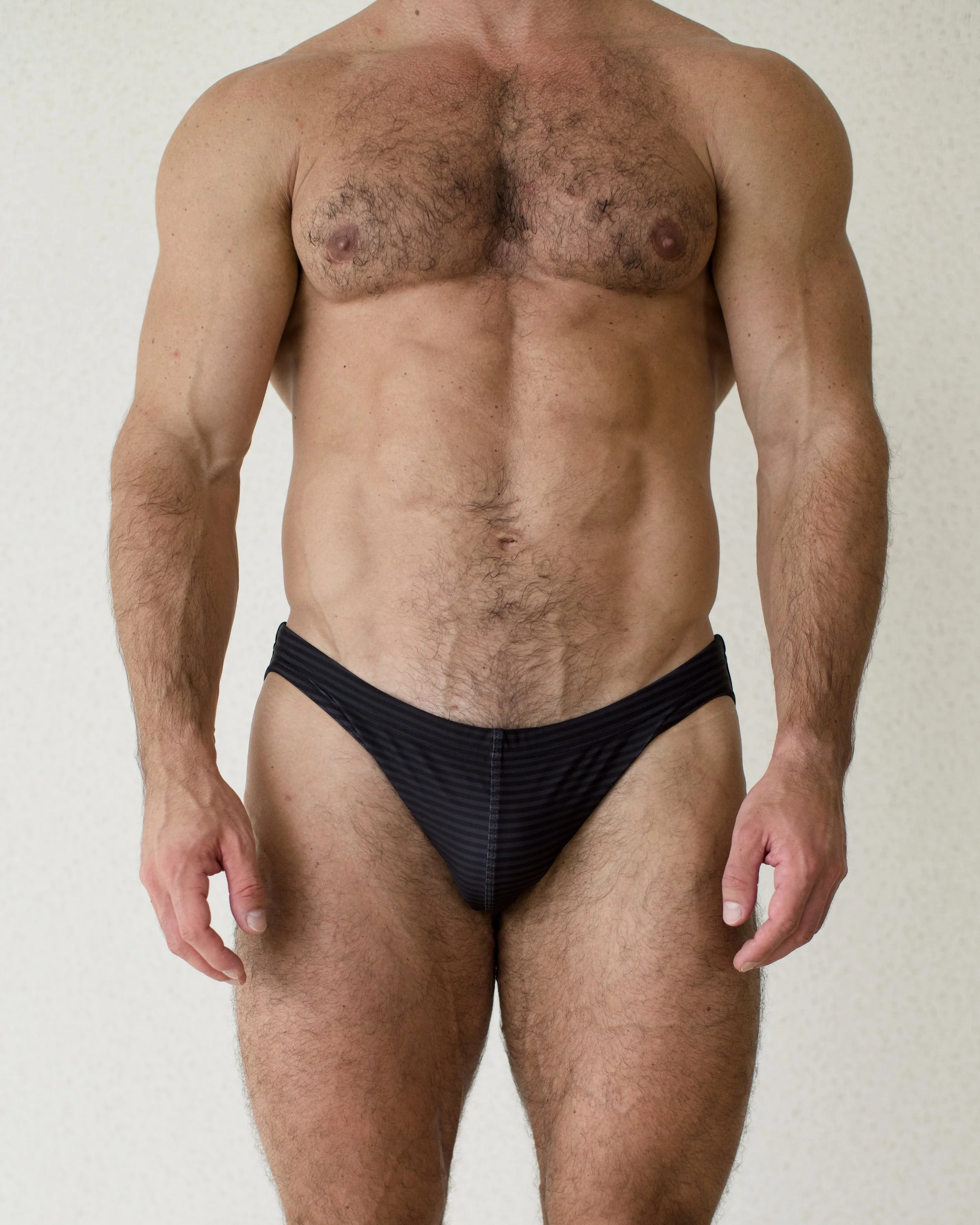 Man seen from front wearing subtly striped black Out of Office swim bikini from Aronik Swim Paradigm collection