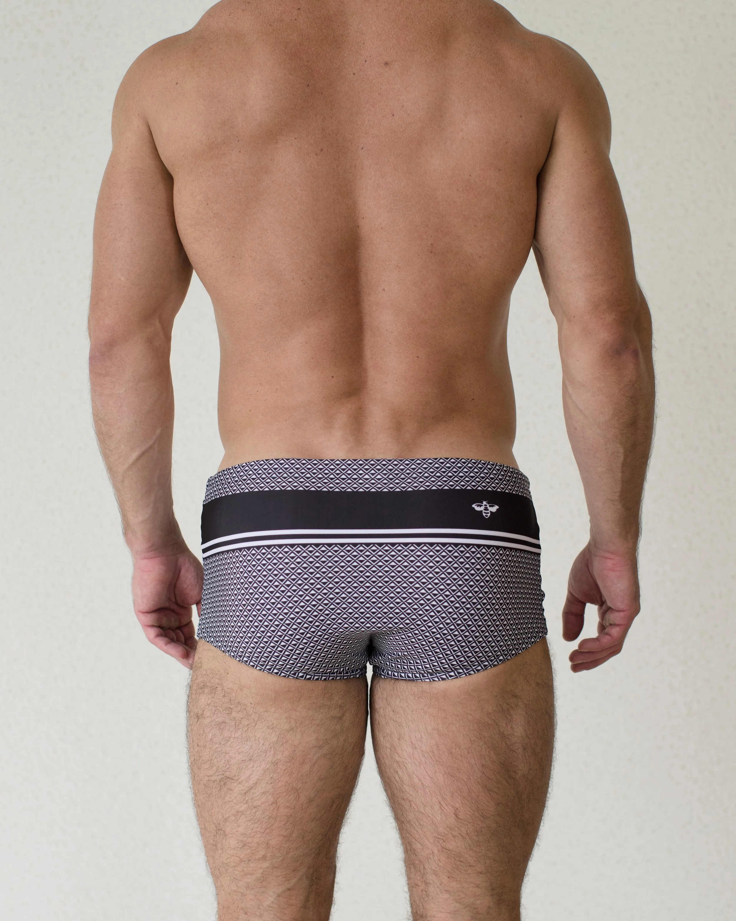 Man seen from back wearing Bastion swim sunga featuring bold black geometric print from Aronik Swim Paradigm Collection