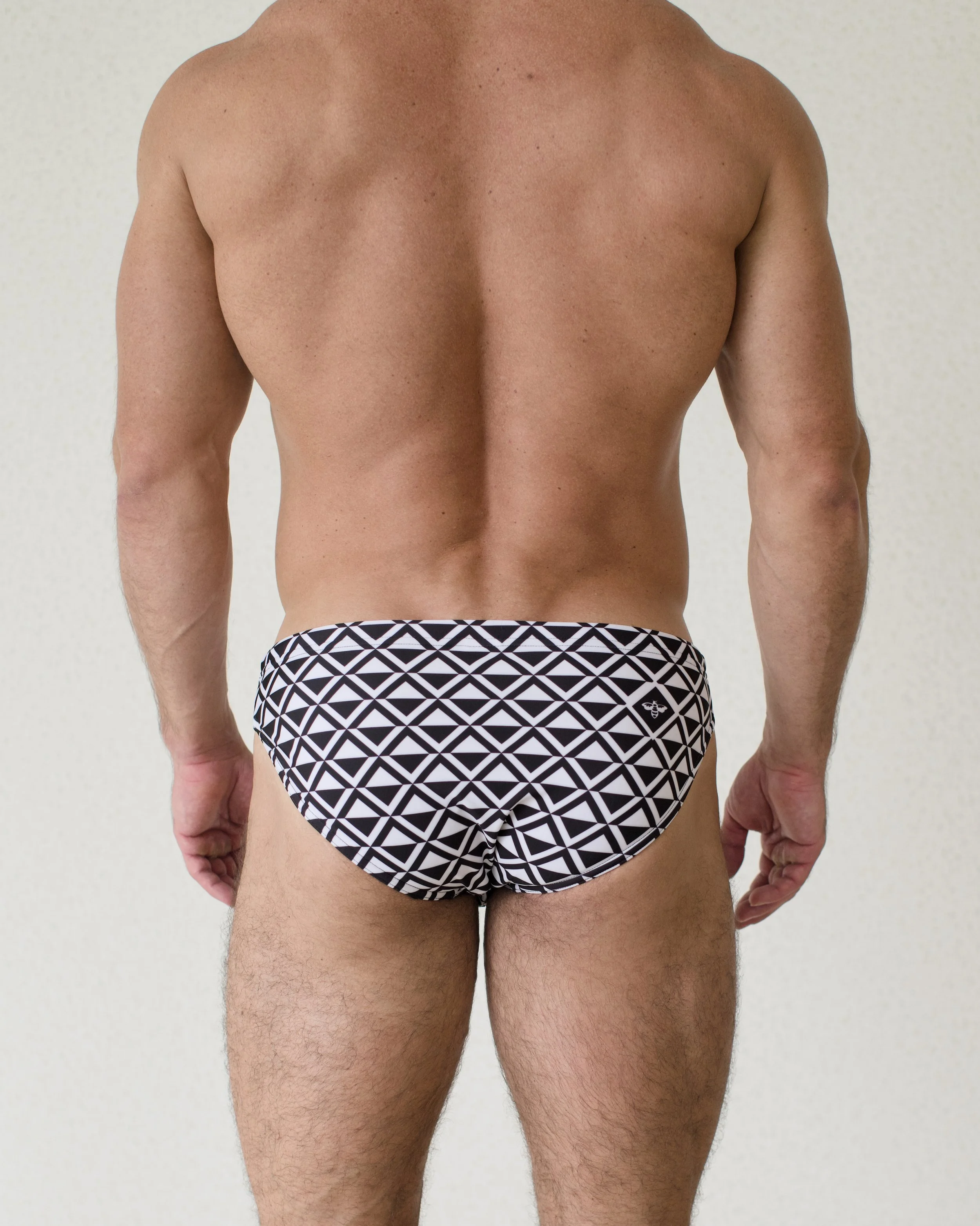 Man seen from back wearing Paradigm swim bikini featuring a black geometric print from Aronik Swim Paradigm Collection