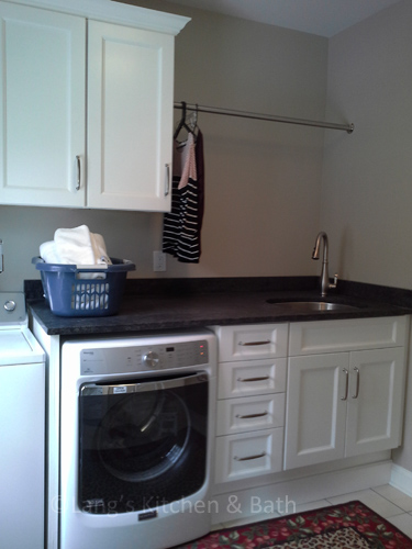 洗衣房设计与白色橱柜，水槽和挂衣服的酒吧。