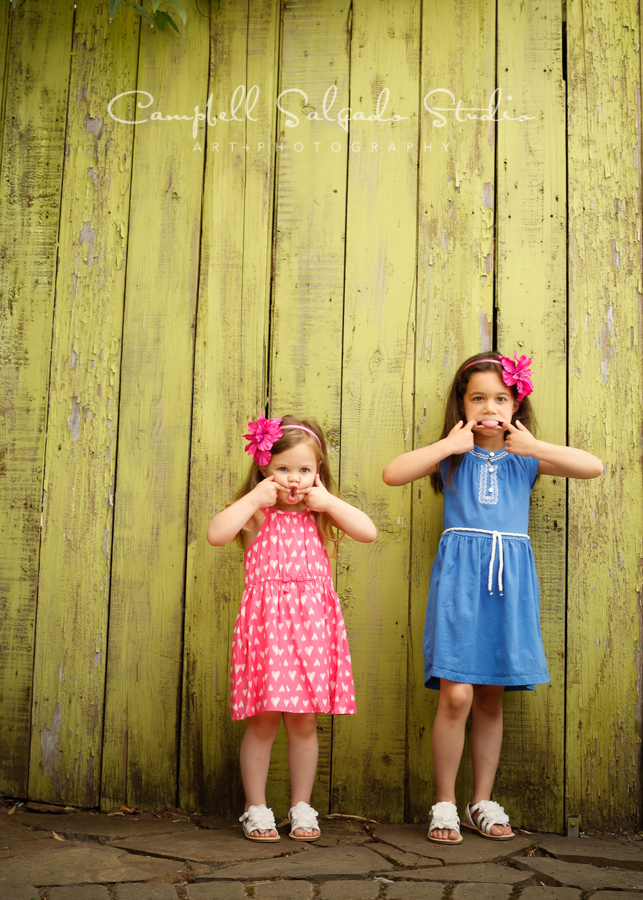  Portrait of sisters&nbsp;on lime fence boards background&nbsp;by family photographers at Campbell Salgado Studio, Portland, Oregon. 