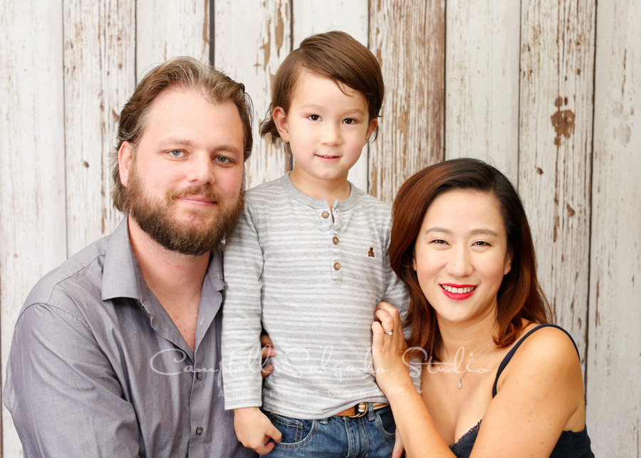  Portrait of family on white fence boards background by family photographers at Campbell Salgado Studio in Portland, Oregon. 