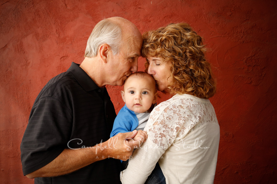  Portrait of grandparents and grandson on red stucco background by family photographers at Campbell Salgado Studio in Portland, Oregon. 