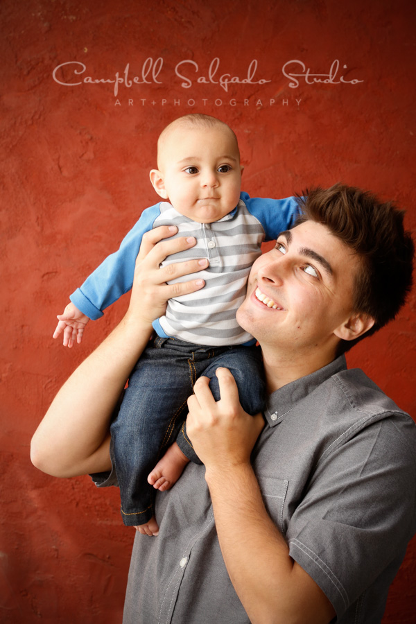  Portrait of father and son on red stucco background by family photographers at Campbell Salgado Studio in Portland, Oregon. 