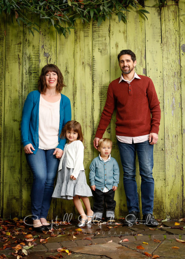  Portrait of family on lime fence boards background by family photographers at Campbell Salgado Studio in Portland, Oregon. 