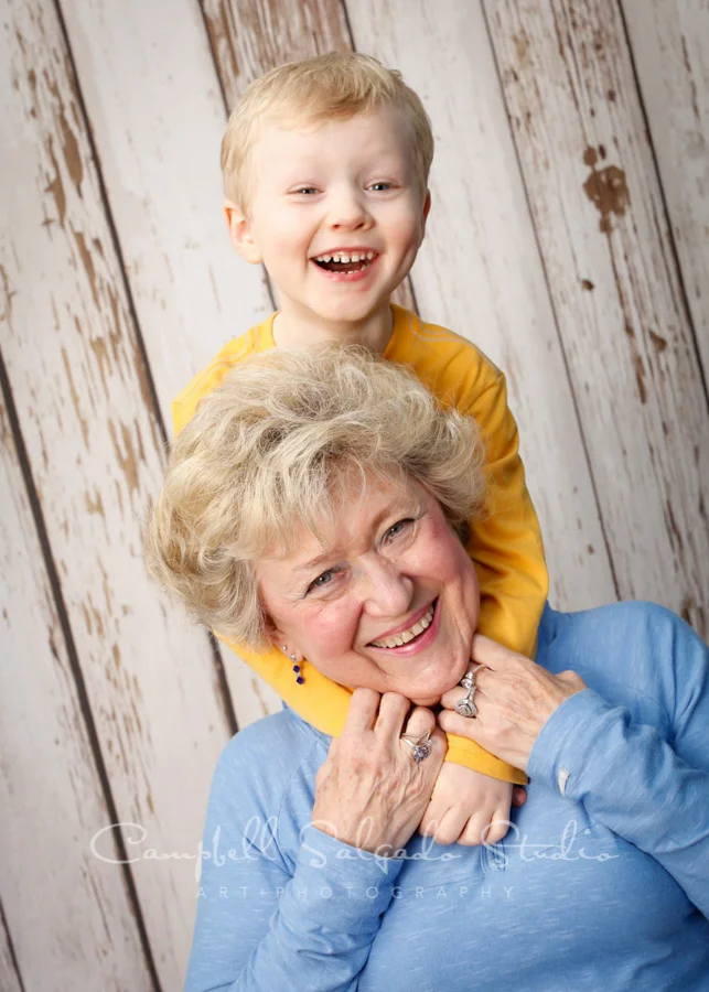 Portrait of grandmother and grandson on white fence boards background by family photographers at Campbell Salgado Studio in Portland, Oregon.