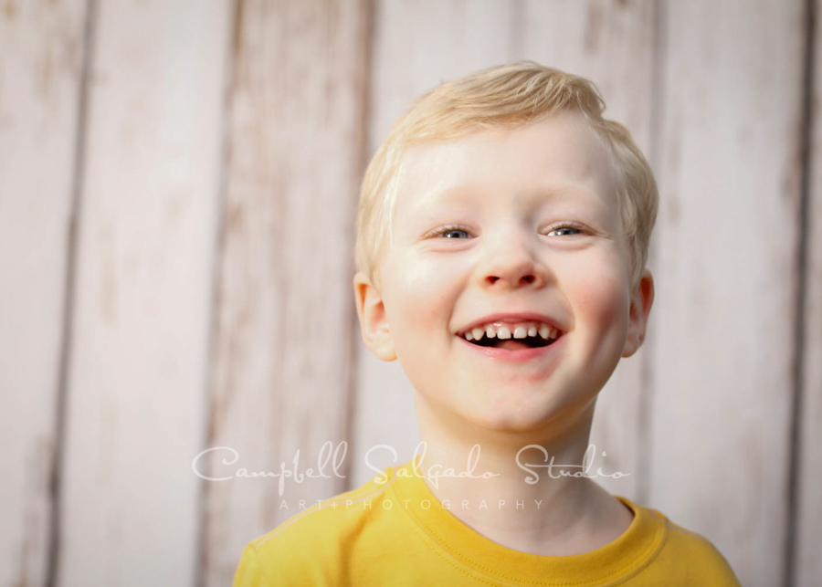  Portrait of boy on white fence boards background by child photographers at Campbell Salgado Studio in Portland, Oregon. 