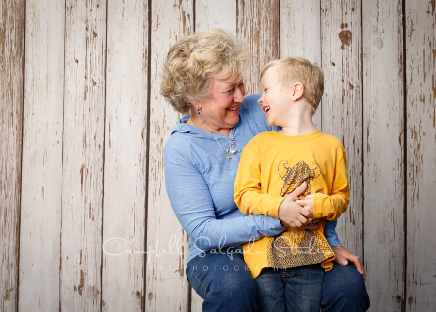  Portrait of grandmother and grandson on white fence boards background by family photographers at Campbell Salgado Studio in Portland, Oregon. 