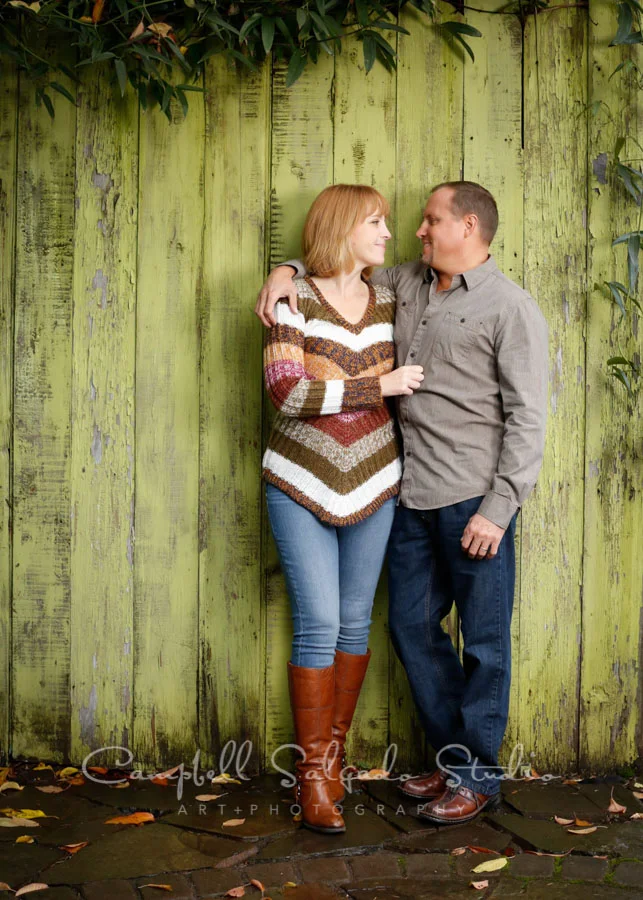 Portrait of couple on lime fence boards background by family photographers at Campbell Salgado Studio in Portland, Oregon.