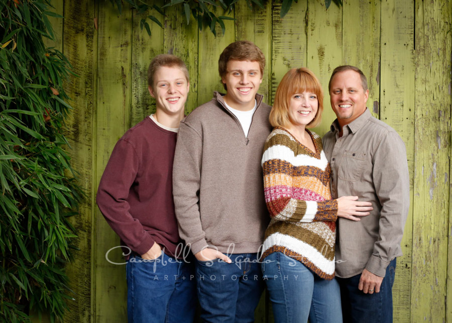  Portrait of family on lime fence boards background by family photographers at Campbell Salgado Studio in Portland, Oregon. 