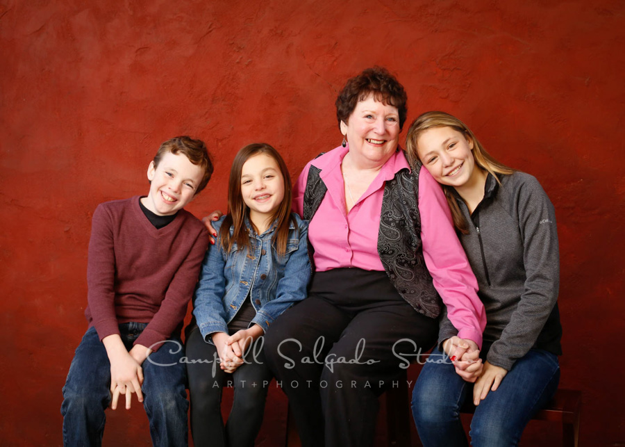  Portrait of grandmother and grandchildren on red stucco background by family photographers at Campbell Salgado Studio in Portland, Oregon. 