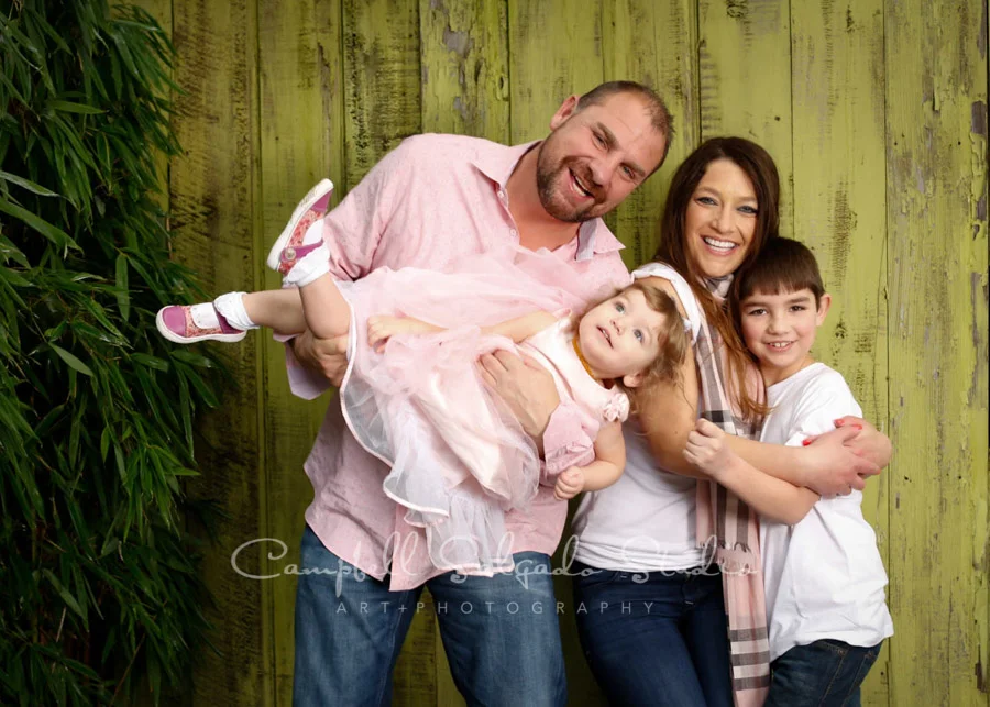Portrait of family on lime fence boards background by family photographers at Campbell Salgado Studio in Portland, Oregon.
