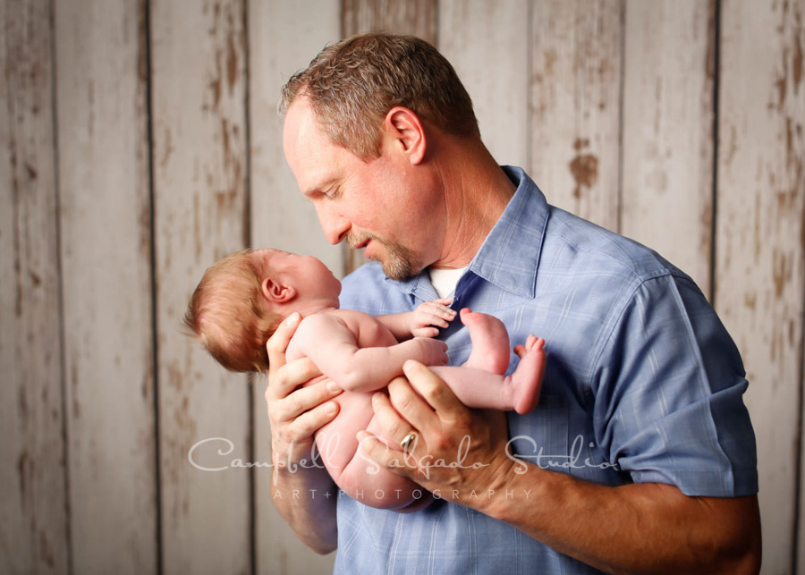  Portrait of father and infant son on white fenceboards background by newborn photographers at Campbell Salgado Studio in Portland, Oregon. 