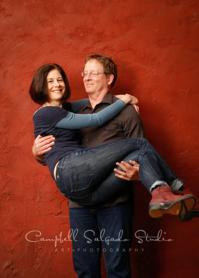 Portrait of couple on red stucco background by couples photographers at Campbell Salgado Studio.