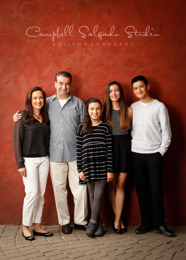 Portrait of family on red stucco background by family photographers at Campbell Salgado Studio in Portland, Oregon.