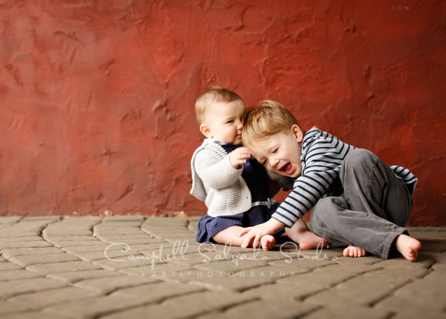  Portrait of children on red stucco background by child photographers at Campbell Salgado Studio in Portland, Oregon. 