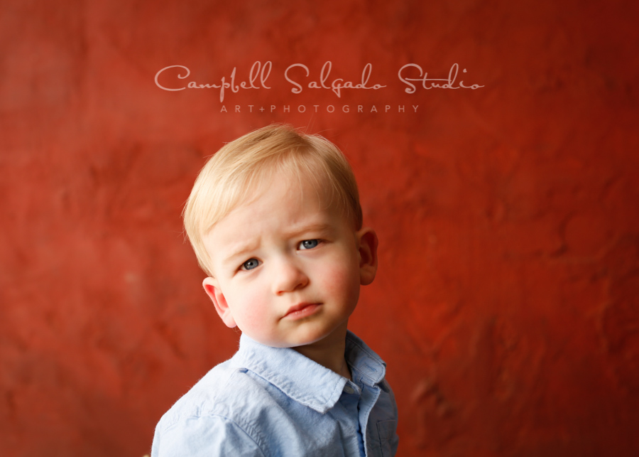  Portrait of child on red stucco background by child photographers at Campbell Salgado Studio in Portland, Oregon. 