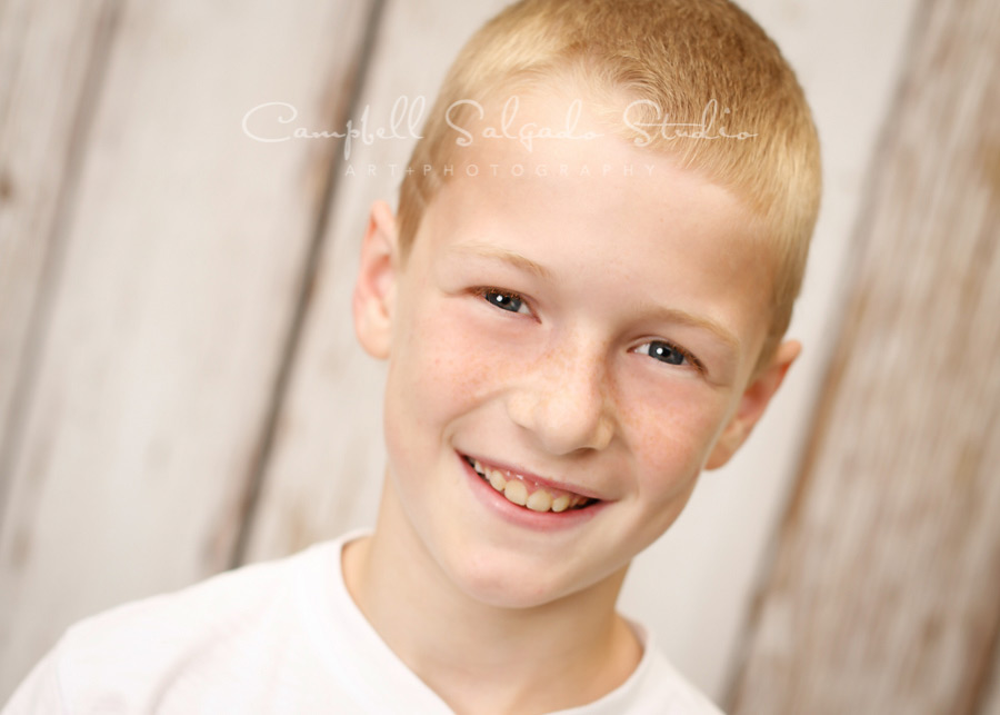  Portrait of boy on white fenceboards background by child photographers at Campbell Salgado Studio in Portland, Oregon. 