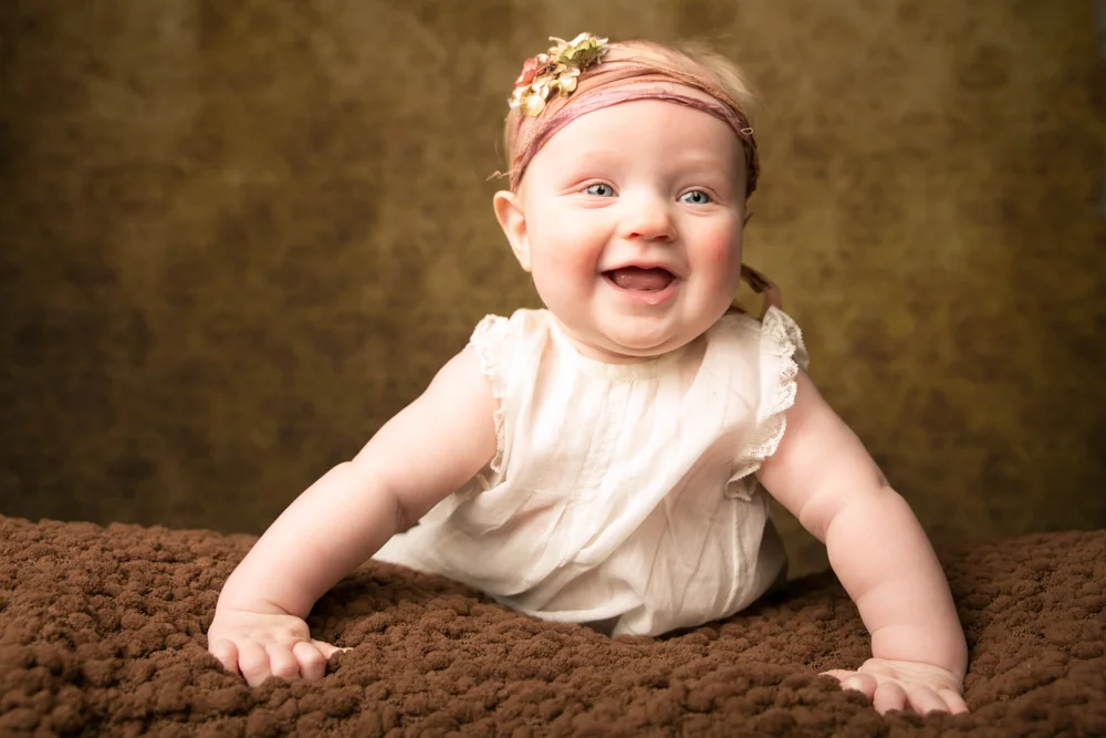 Three month baby photography of baby girl lying on belly against amber light (gold) background in a portrait from Campbell Salgado Studio in Portland, Oregon.