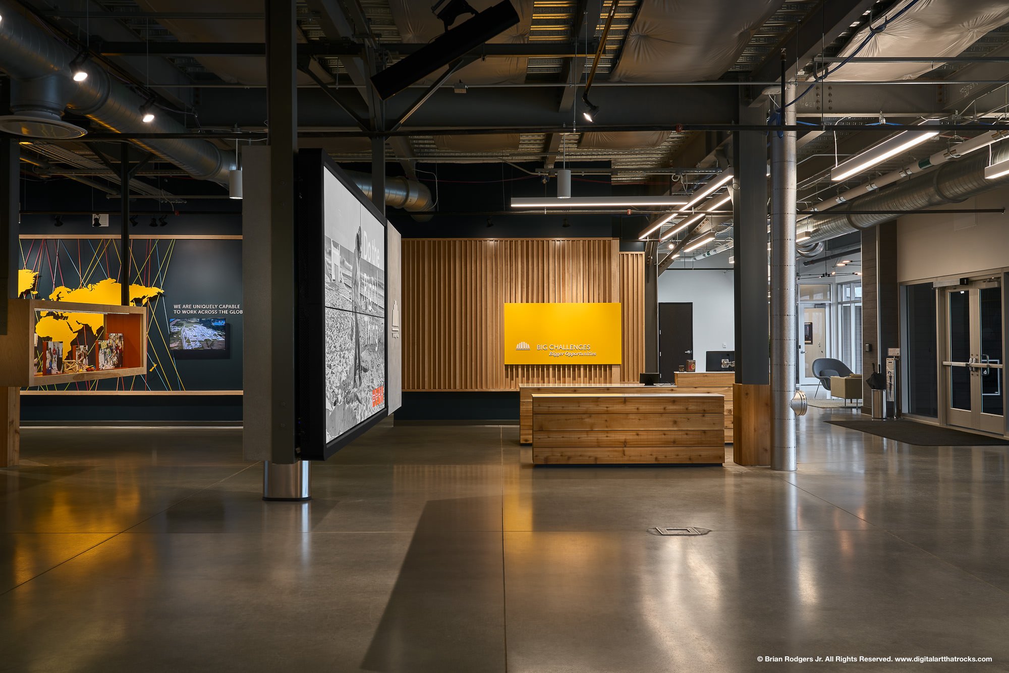 Open-concept corporate office interior photography featuring industrial ceilings, polished concrete floors, and digital signage at the Heritage Group in Indianapolis, Indiana for workplace design and fit-out companies.