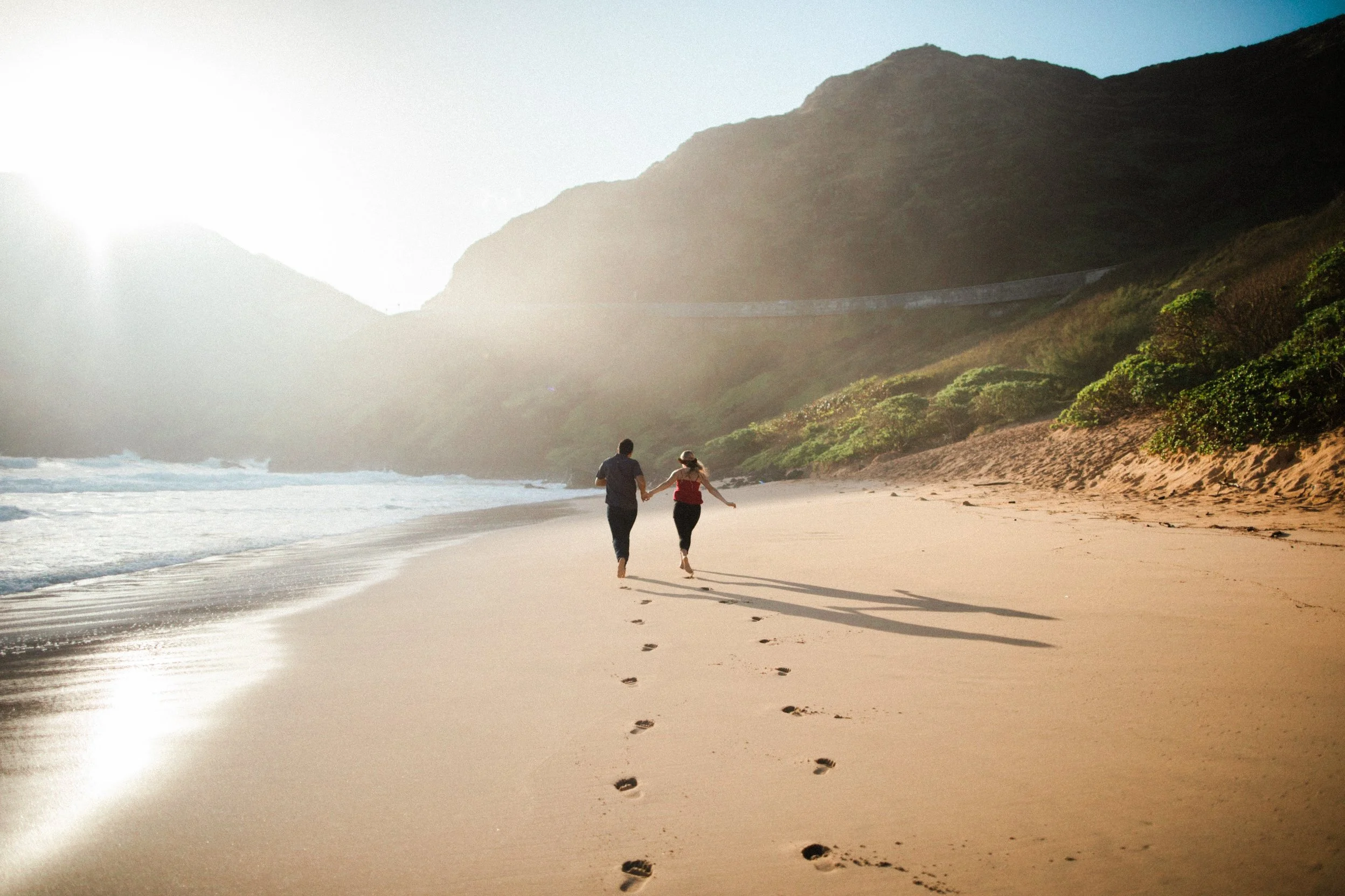 A couple walking hand during their engagement session in Hawaii at sunrise at Makapuu