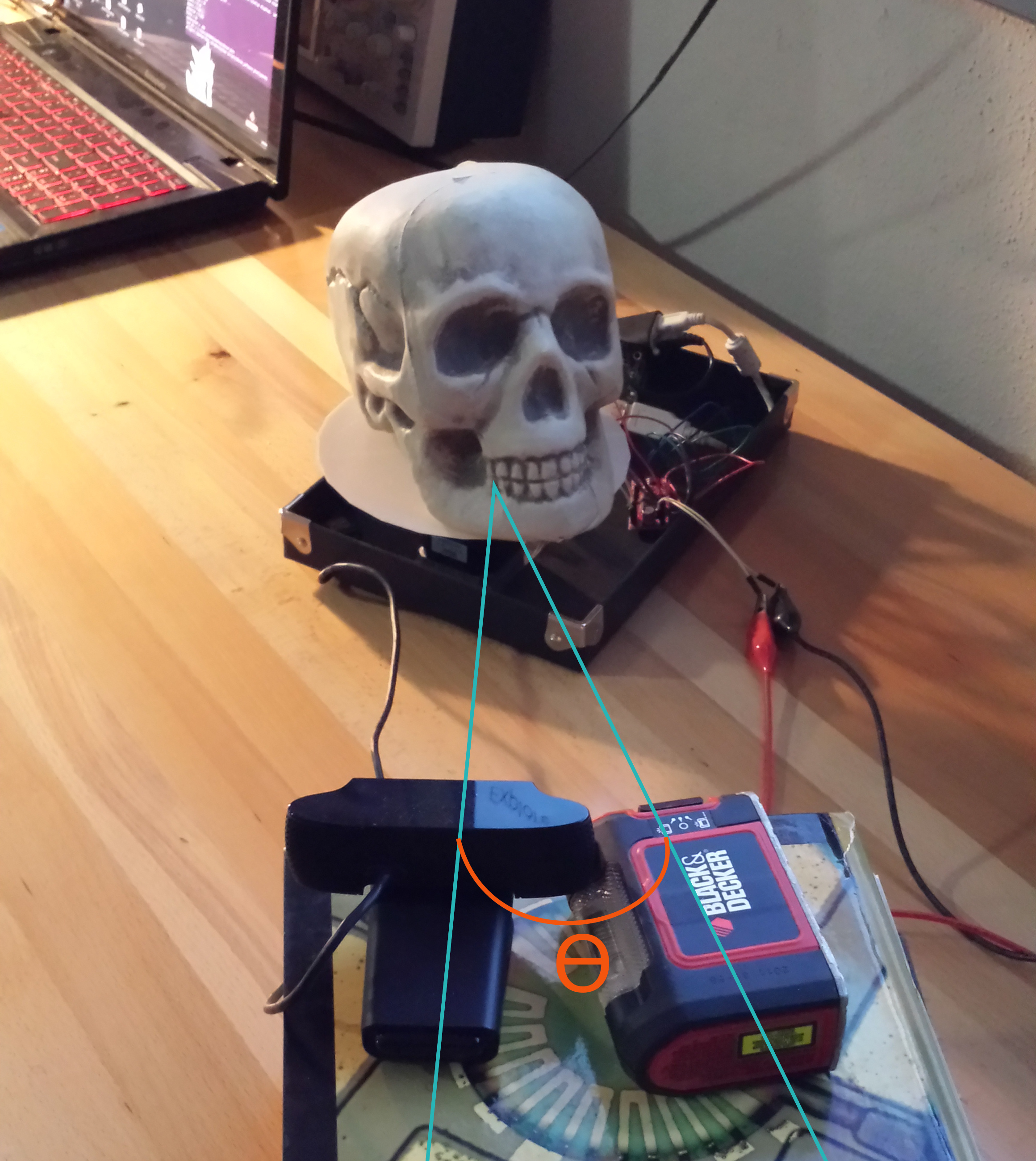 The arrangement of hardware components. The embedded linux device, stepper motor driver, and stepper motor are placed in an upside-down box lid, and the camera/laser are resting on a stack of textbooks. Choose a camera/laser height which allows the laser to best fill the cavities of the device being scanned. Ө (Theta) defines the angle between the center of the camera's field of vision and the plane of the laser.