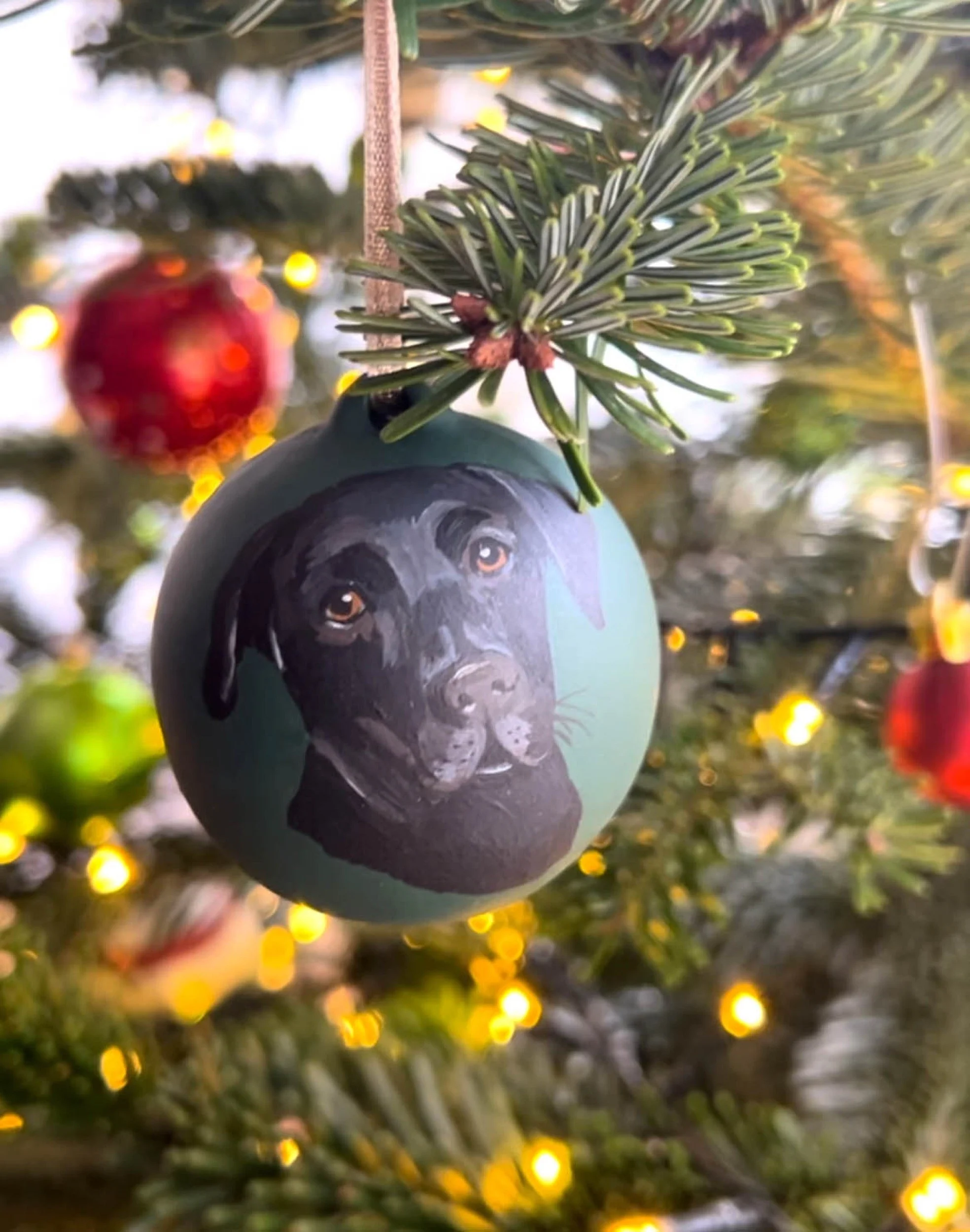 Hand-painted personalised dog portrait Christmas bauble against a festive tree background