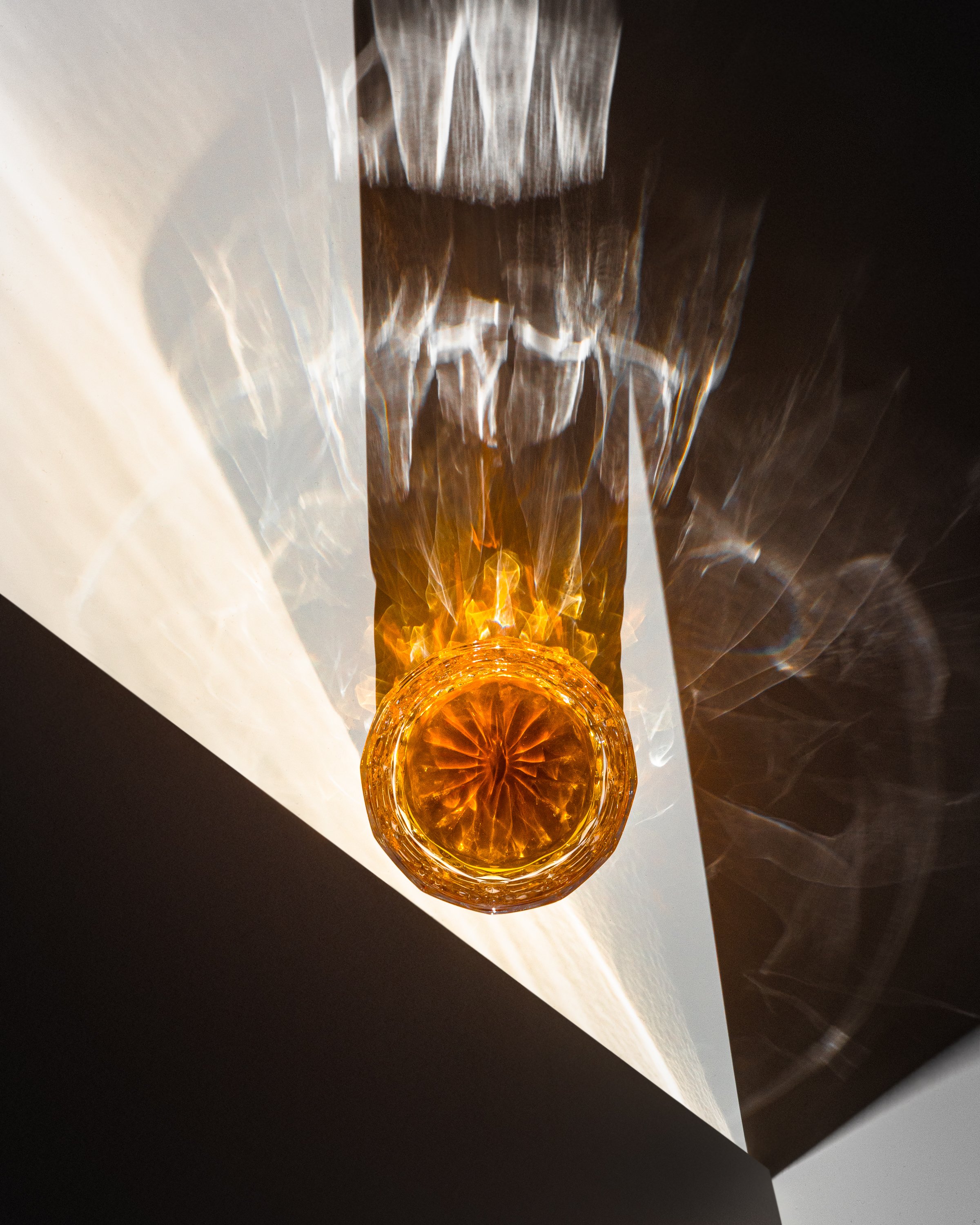 top-down view of whiskey in a crystal tumbler being lit from the side by low, hard light resulting in complex shadows and refraction