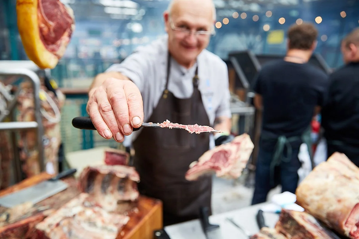 Image of a chef holding out a knife with a sample of meat on it. Taken at a food festival.