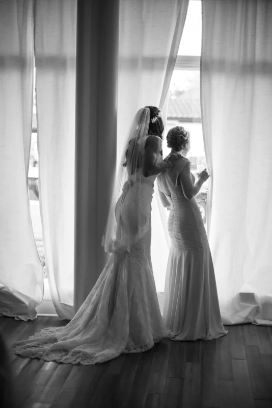Bride and bride's maid peek out the window at the White Room on her wedding day.