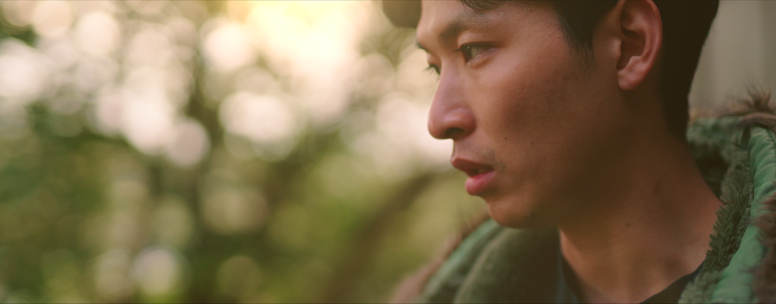 Close-up of a young man in military camouflage looking thoughtfully into the distance, with a blurred natural outdoor background.