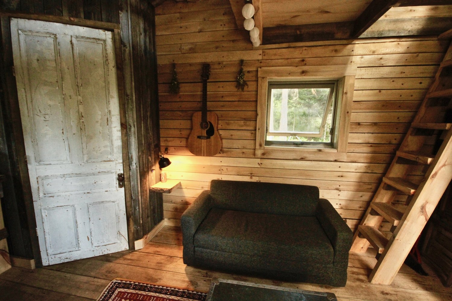 La pi&egrave;ce principale&nbsp;: une porte blanche r&eacute;cup&eacute;r&eacute;e, une guitare au mur, un divan et l&rsquo;&eacute;chelle de la mezzanine