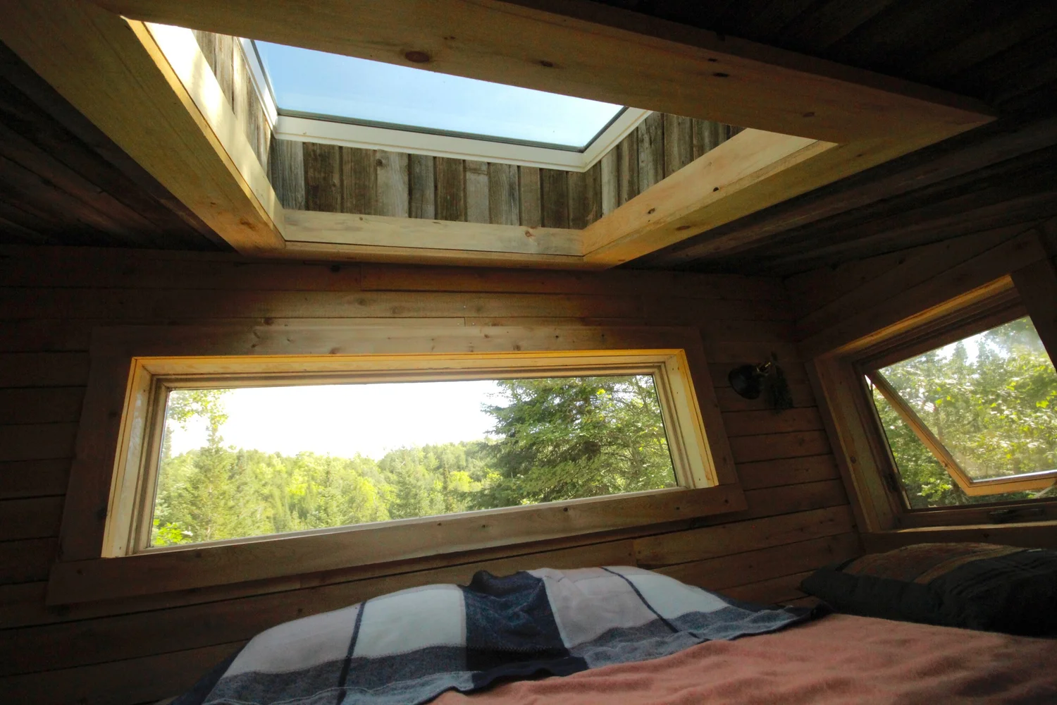 Le lit en mezzanine sous le puits de lumi&egrave;re, avec une longue fen&ecirc;tre qui donne sur les arbres