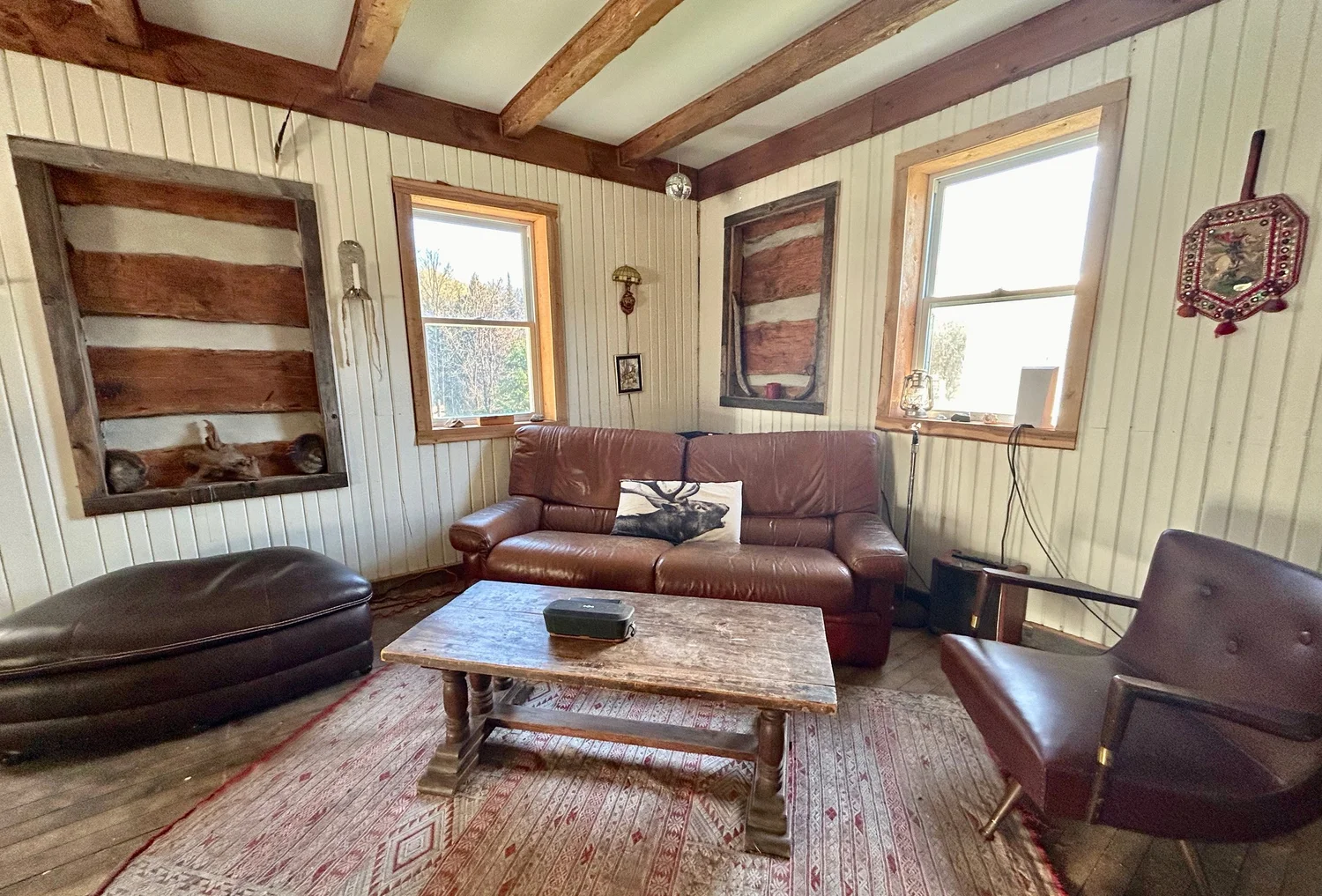 Salon avec deux divans de cuir, une lourde table basse en bois et des poutres de plafond &eacute;quarries &agrave; la main
