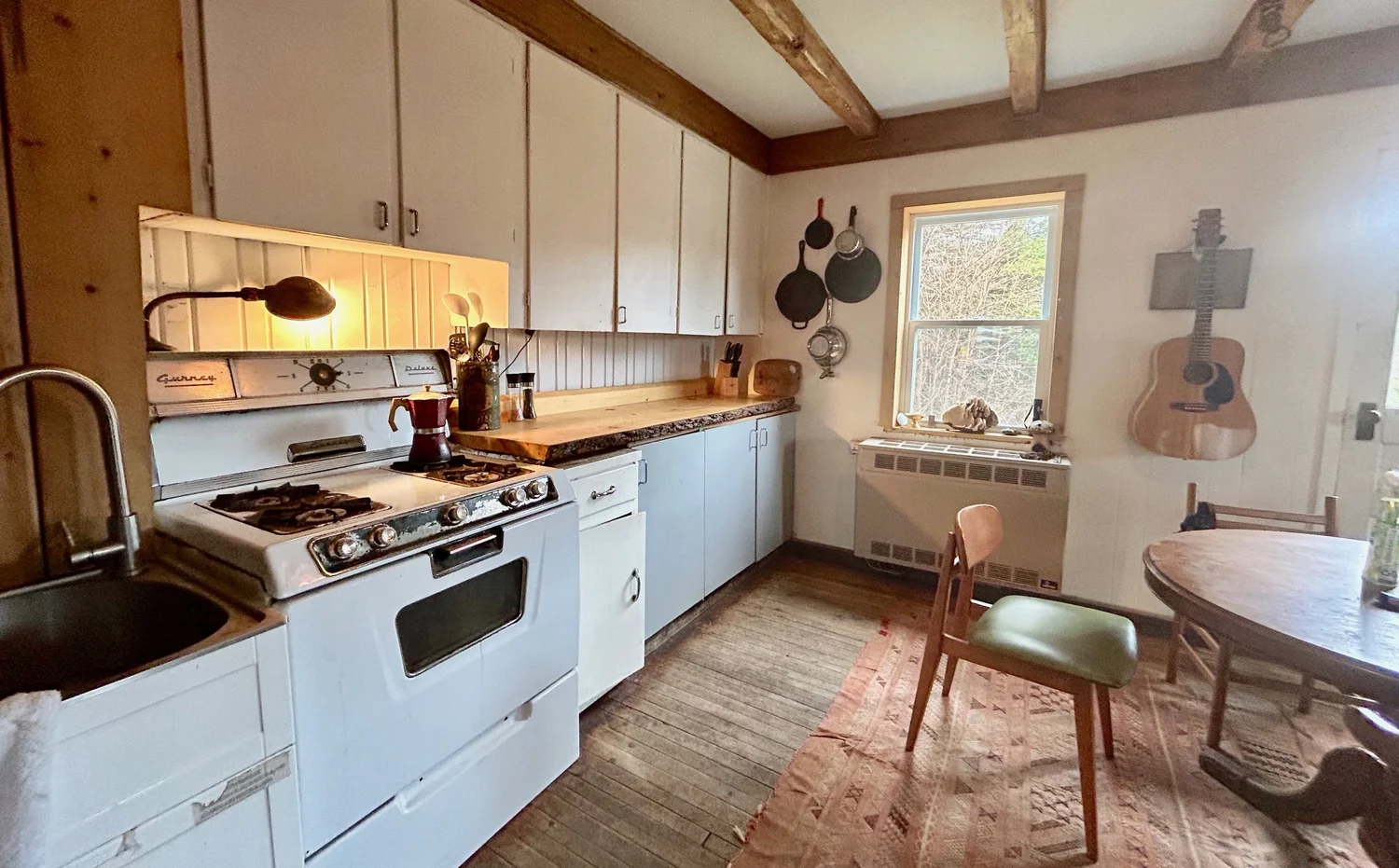 Cuisine avec une cuisini&egrave;re blanche, un &eacute;vier profond, un comptoir de bois et des armoires le long du mur de fen&ecirc;tres
