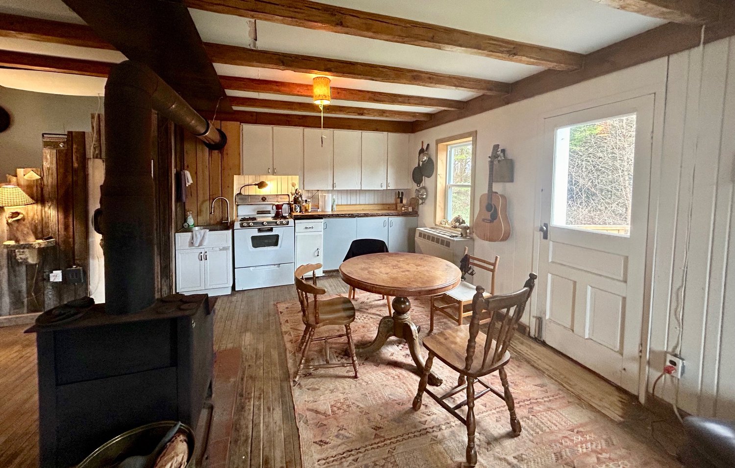 Le po&ecirc;le &agrave; bois &agrave; l&rsquo;avant-plan, la table &agrave; manger et la porte ext&eacute;rieure derri&egrave;re