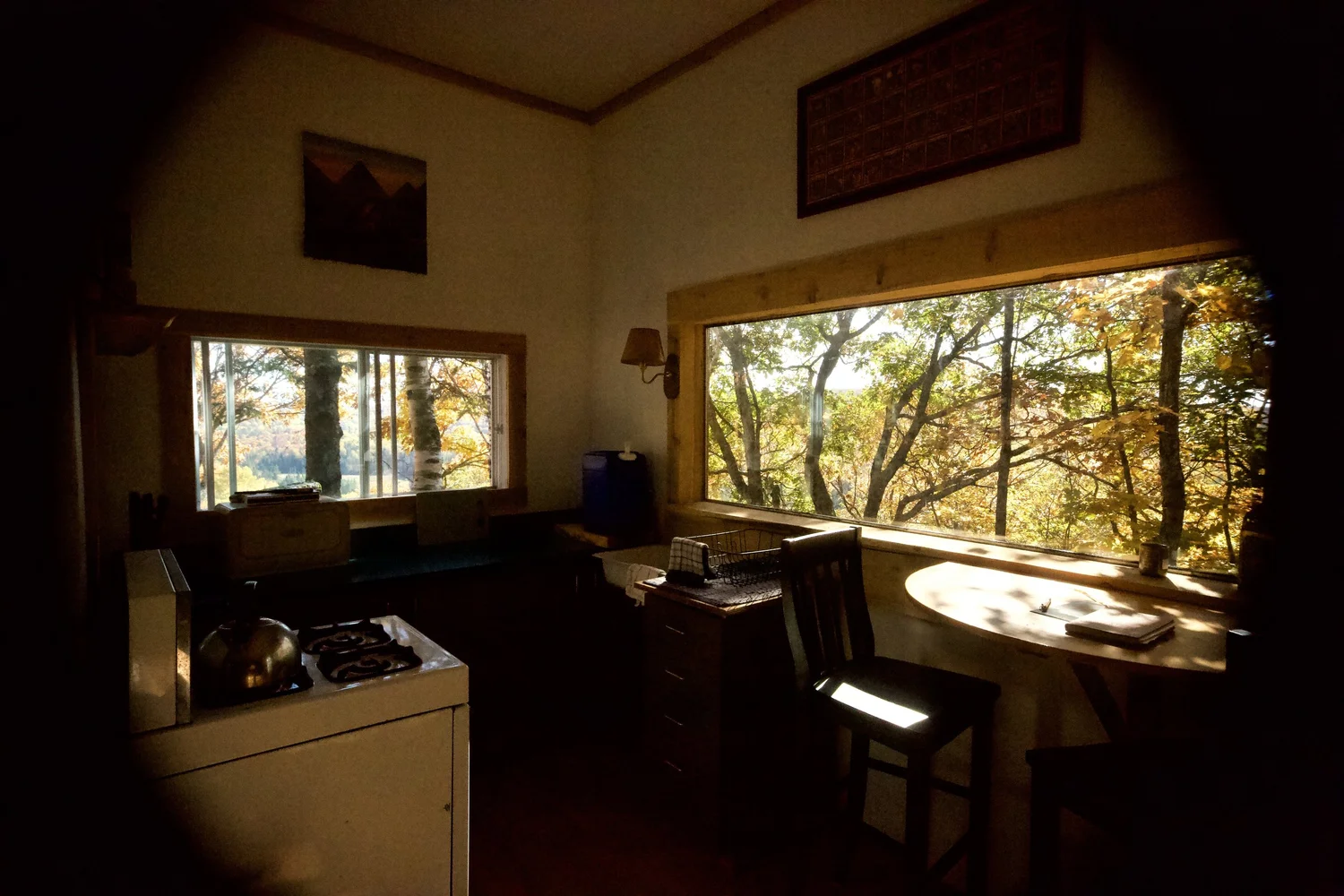 La table en demi-lune sous la baie vitrée, une chaise approchée, les arbres d’automne qui remplissent la vitre