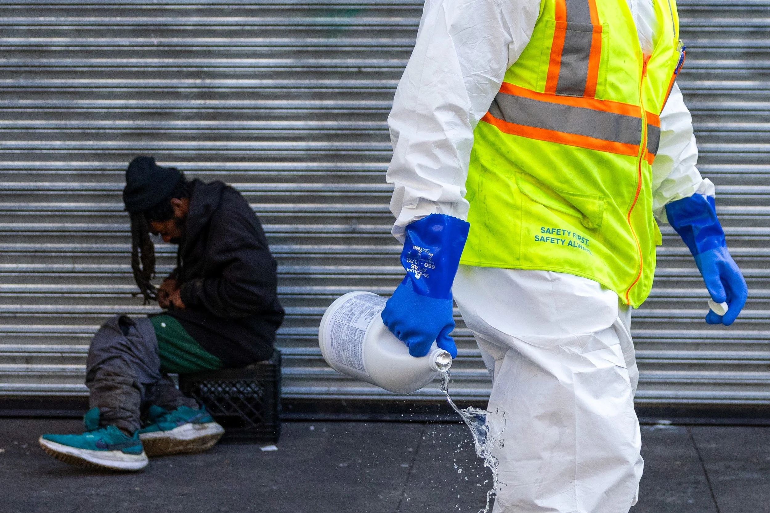A Department of Public Works employee puts cleaning chemicals near a person sitting on a street at the corridor near 6th Street and Market in San Francisco on Thursday, July 10, 2025. This stretch of the Tenderloin has seen improvements, but at nigh
