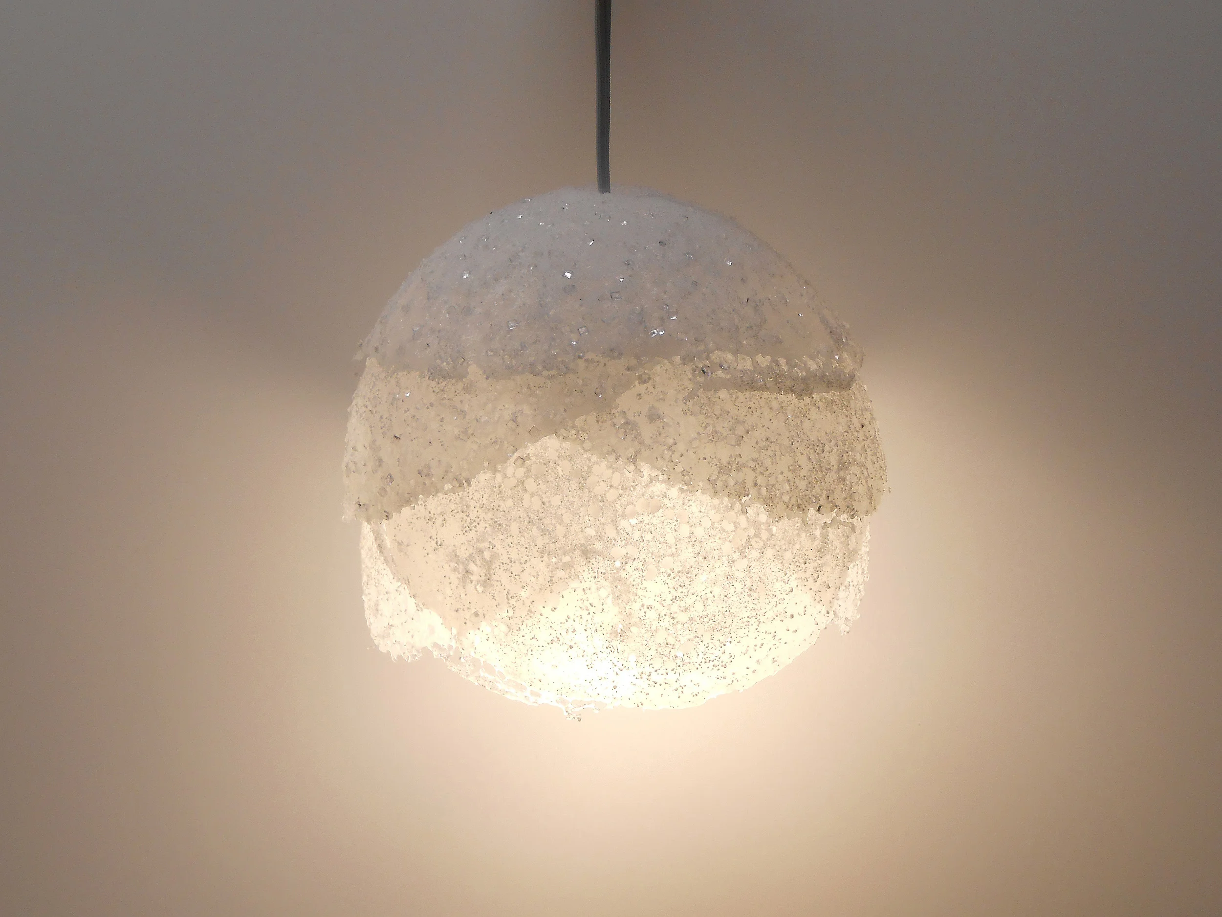 Molten Lamps utilize raw low-density polyethylene pellets and a hand-crafted process to create pendants of subtly varied forms. Raw pellets are heated and fused from the inside out allowing the texture of the material to be maintained on the exterior. The hemispherical shades are then layered creating a gradient of opacity from top to bottom.